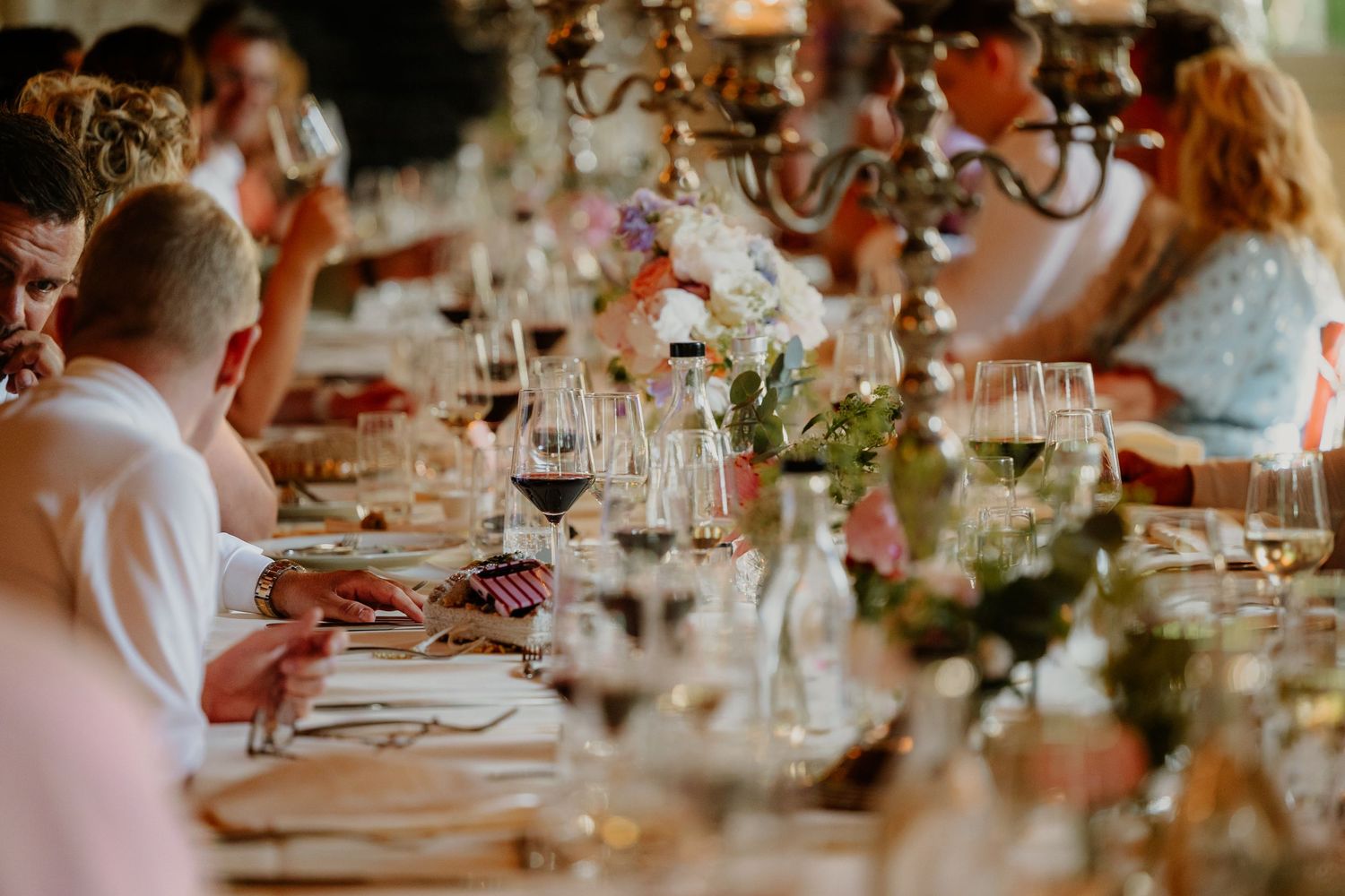 Gasten aan een lange sfeervol gedekte tafel tijdens het bruiloftsdiner