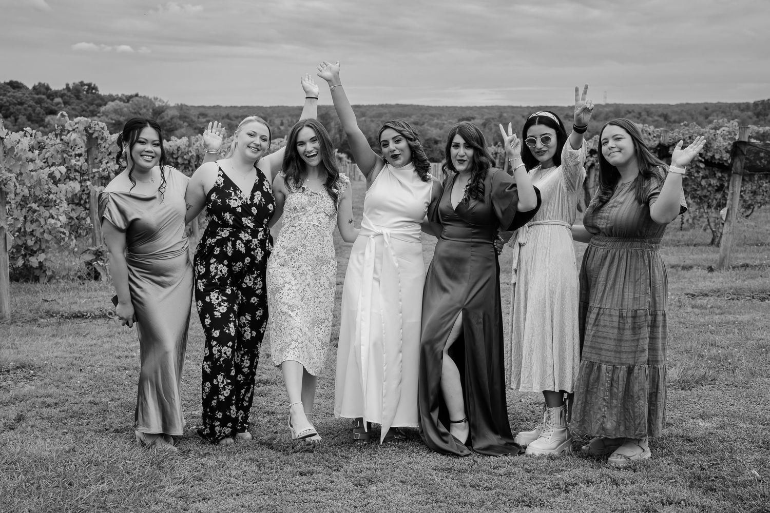 Black and white photo of seven women in elegant dresses celebrating outdoors at a vineyard wedding.