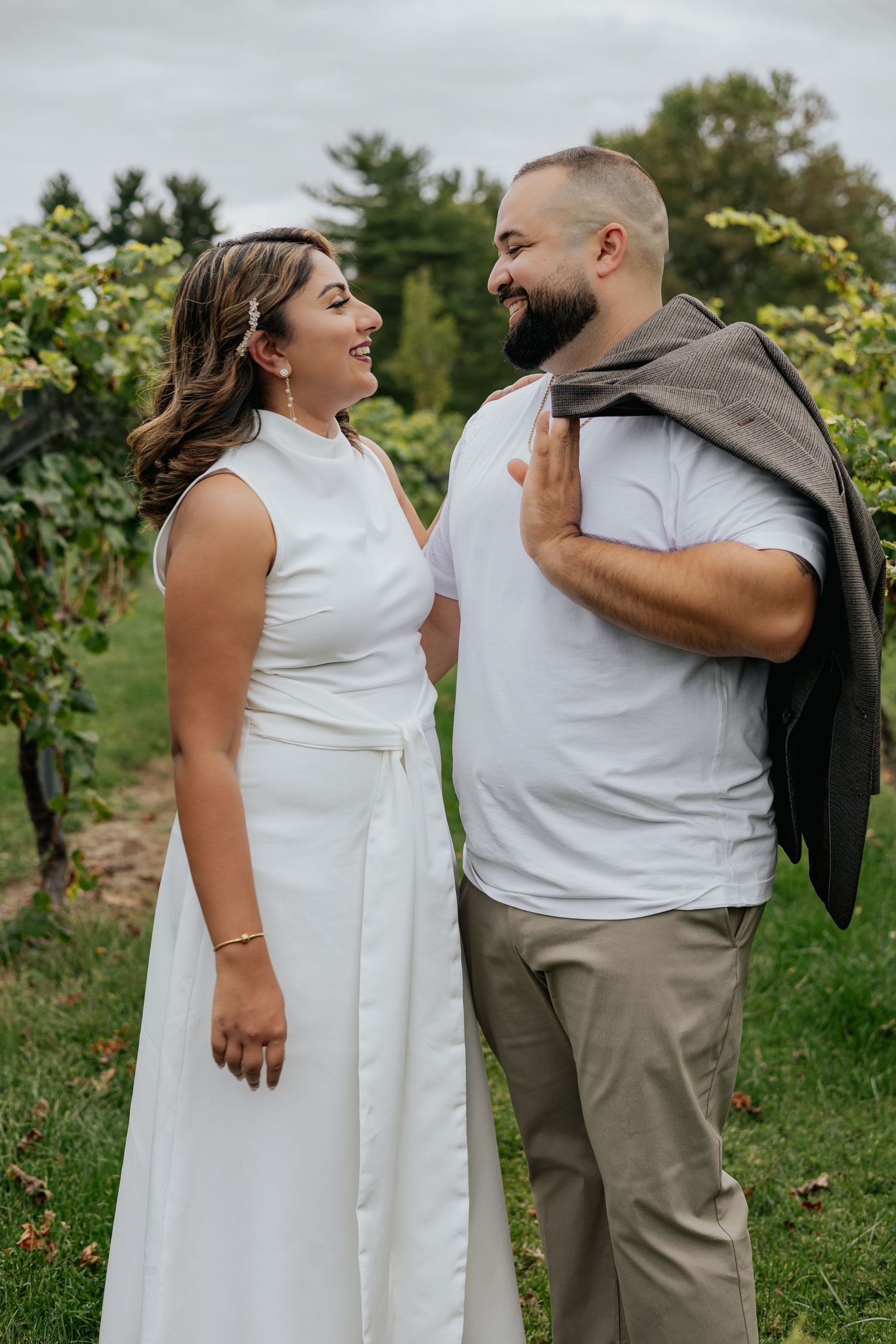 Laughing couple in a vineyard, man holding jacket over shoulder in white shirt and khakis.