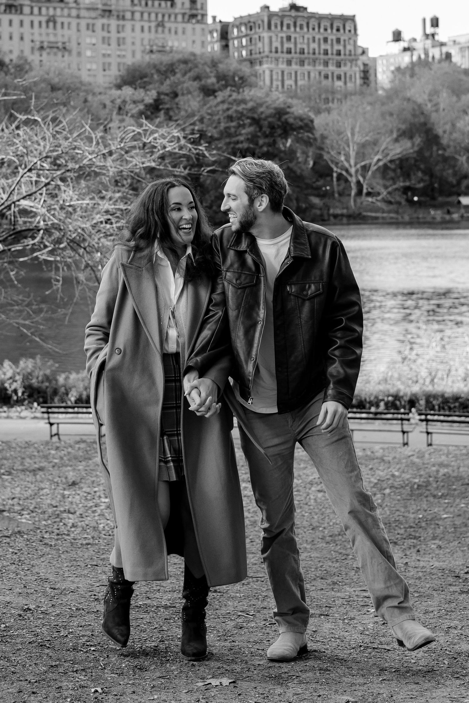 Black and white photo of laughing couple holding hands walking in Central Park in fall.