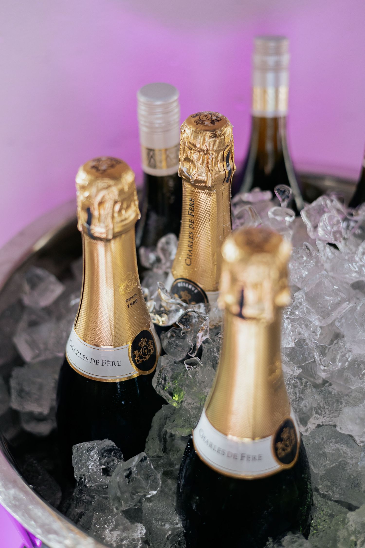 Three Charles de Fere champagne bottles chilling in ice bucket against purple background.