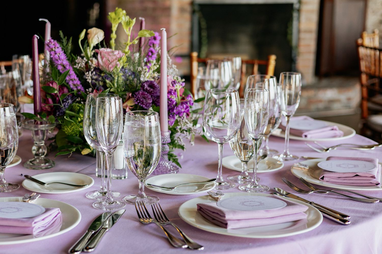 Elegant table setting with purple napkins, crystal glasses, and vibrant purple floral centerpiece.
