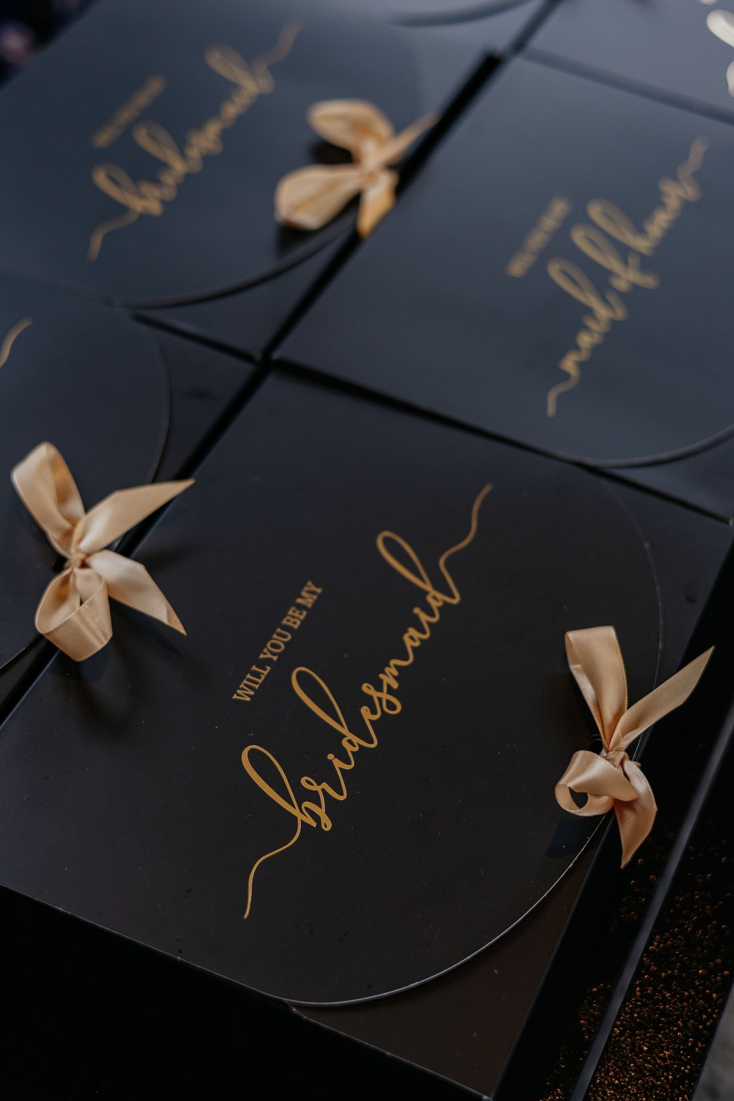Elegant black bridesmaid proposal boxes with gold script and champagne satin ribbons.
