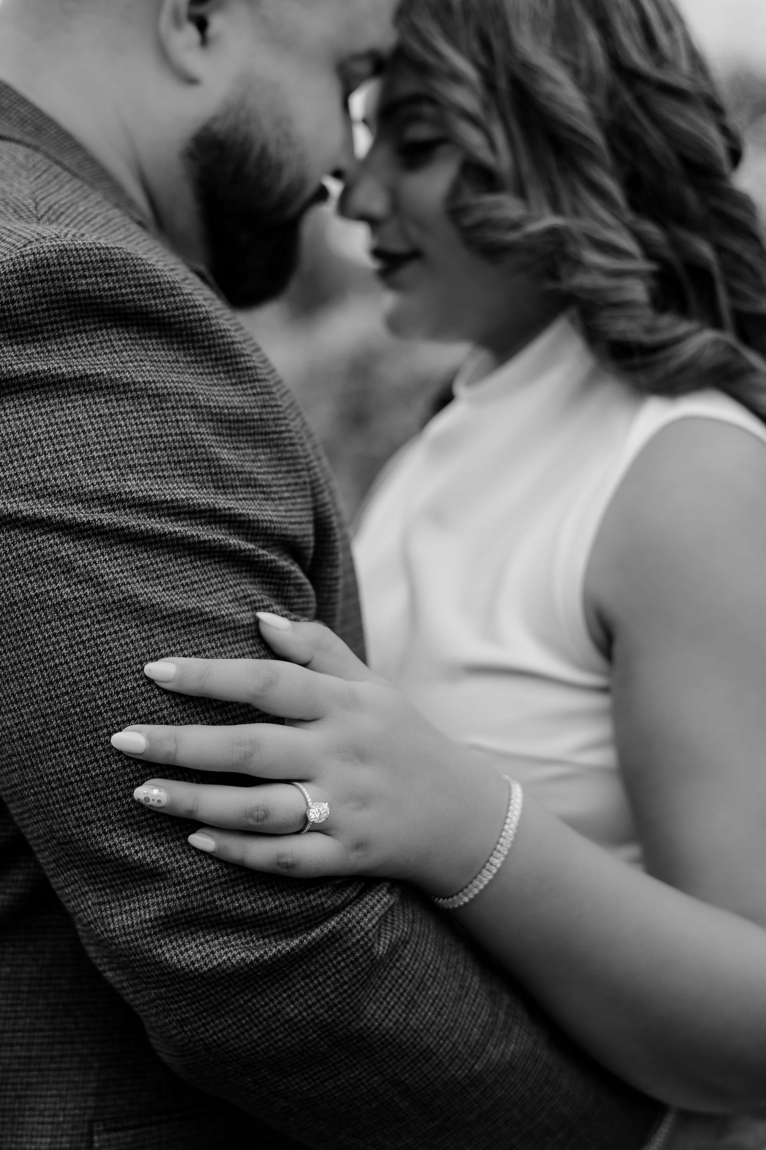 Close-up black and white photo of couple almost kissing, bride's diamond engagement ring prominently displayed.