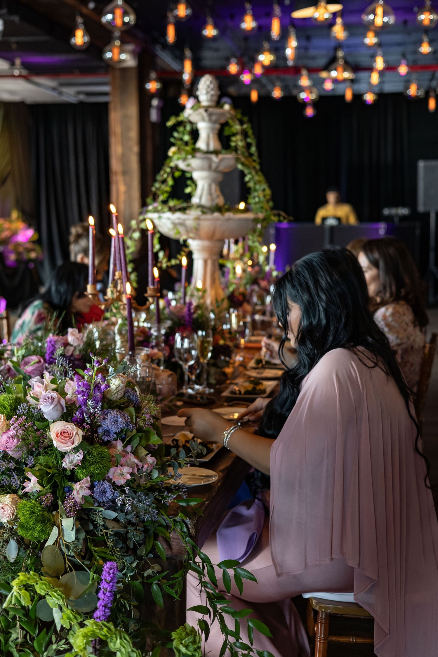 Pregnant woman in pink gown seated at lavishly decorated baby shower table with fountain centerpiece.