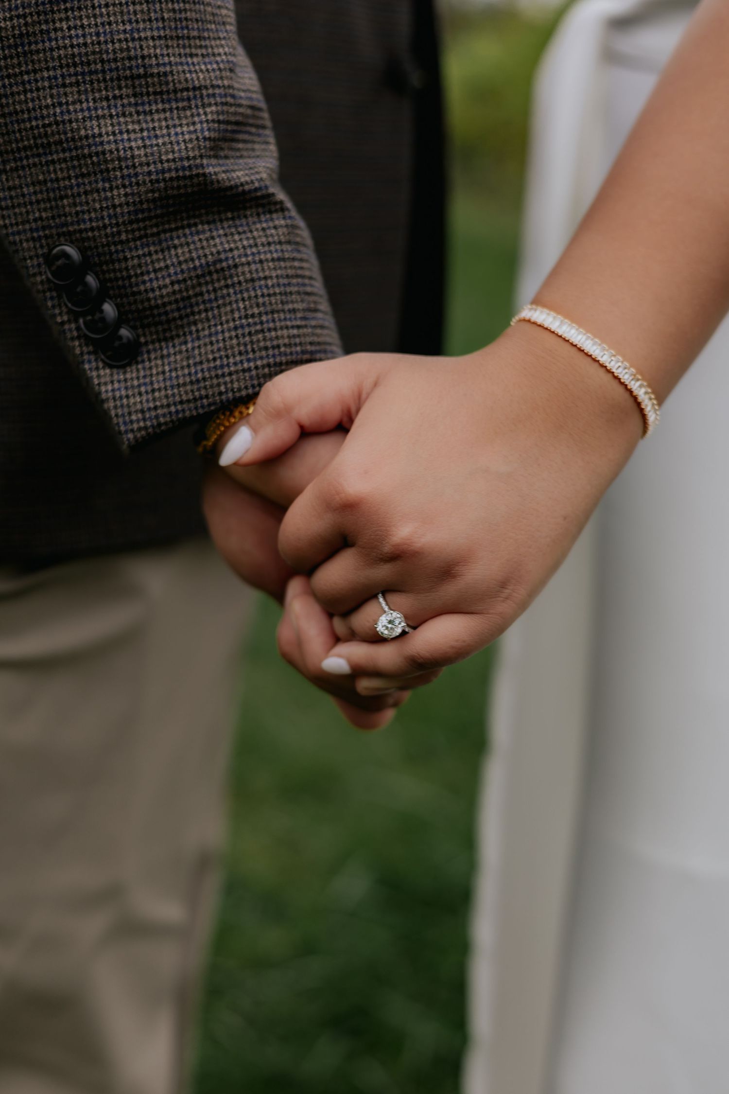 Close-up of couple holding hands, bride wearing a stunning diamond halo engagement ring and tennis bracelet.