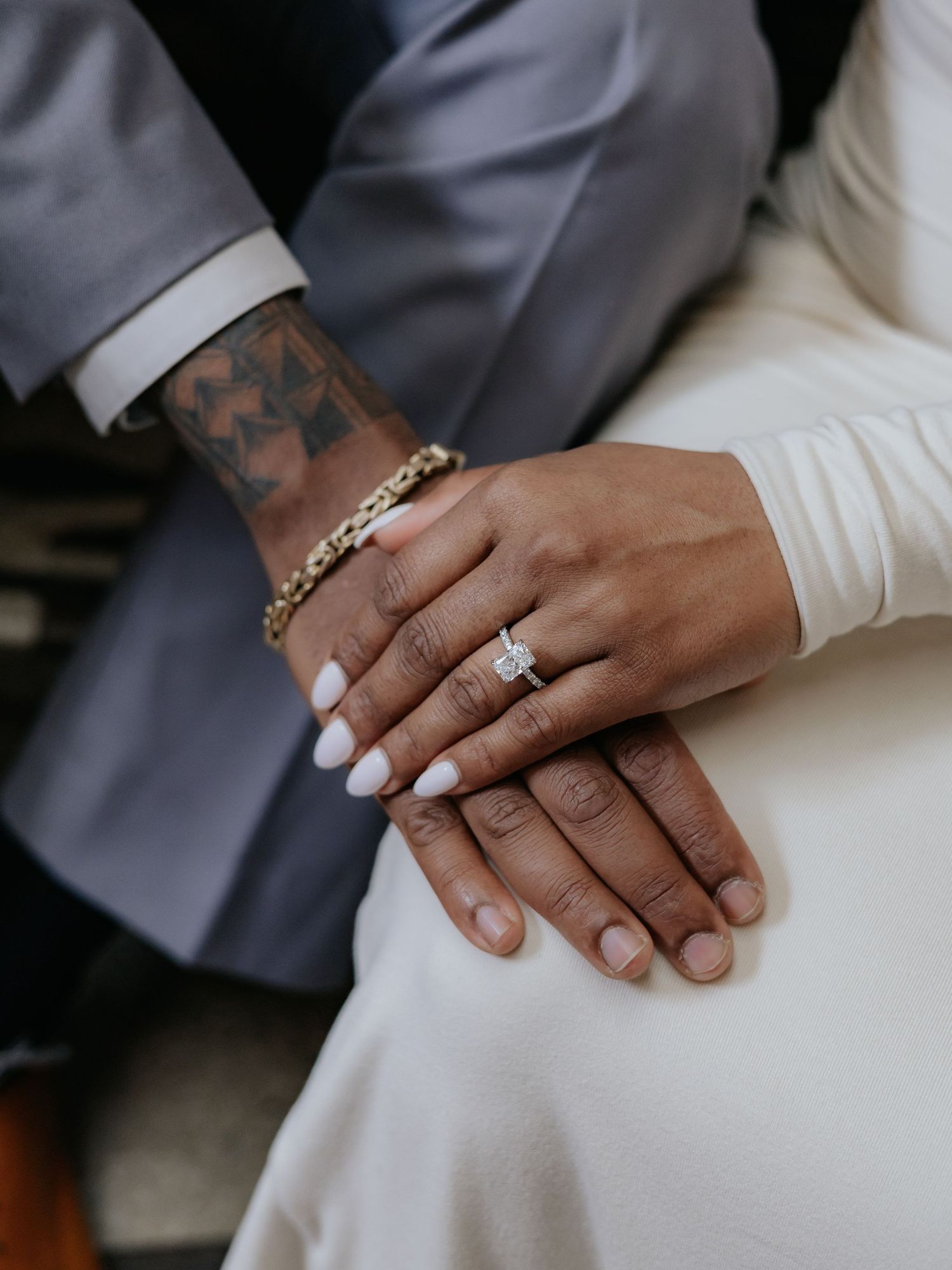 Close-up of engaged couple's hands showing diamond engagement ring, man with tattoos and gold bracelet.