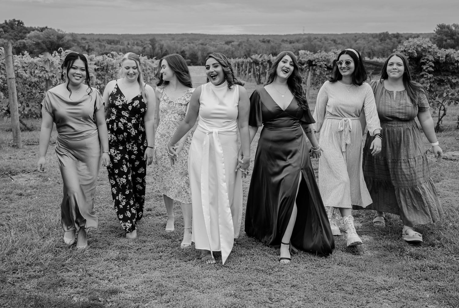 Black and white photo of seven women in formal dresses walking together at a vineyard wedding.