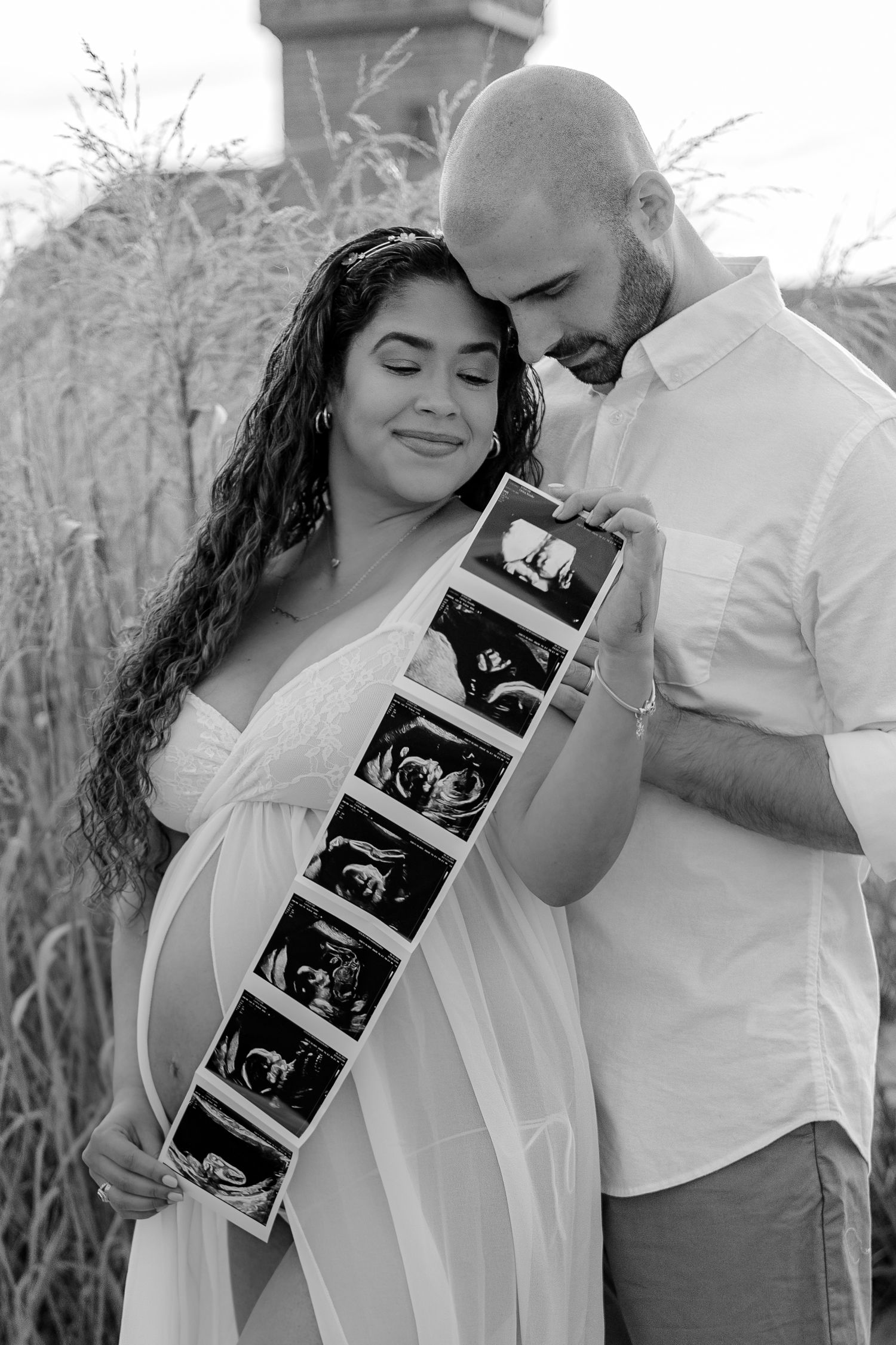Black and white photo of expecting couple holding ultrasound strip on beach during maternity shoot.