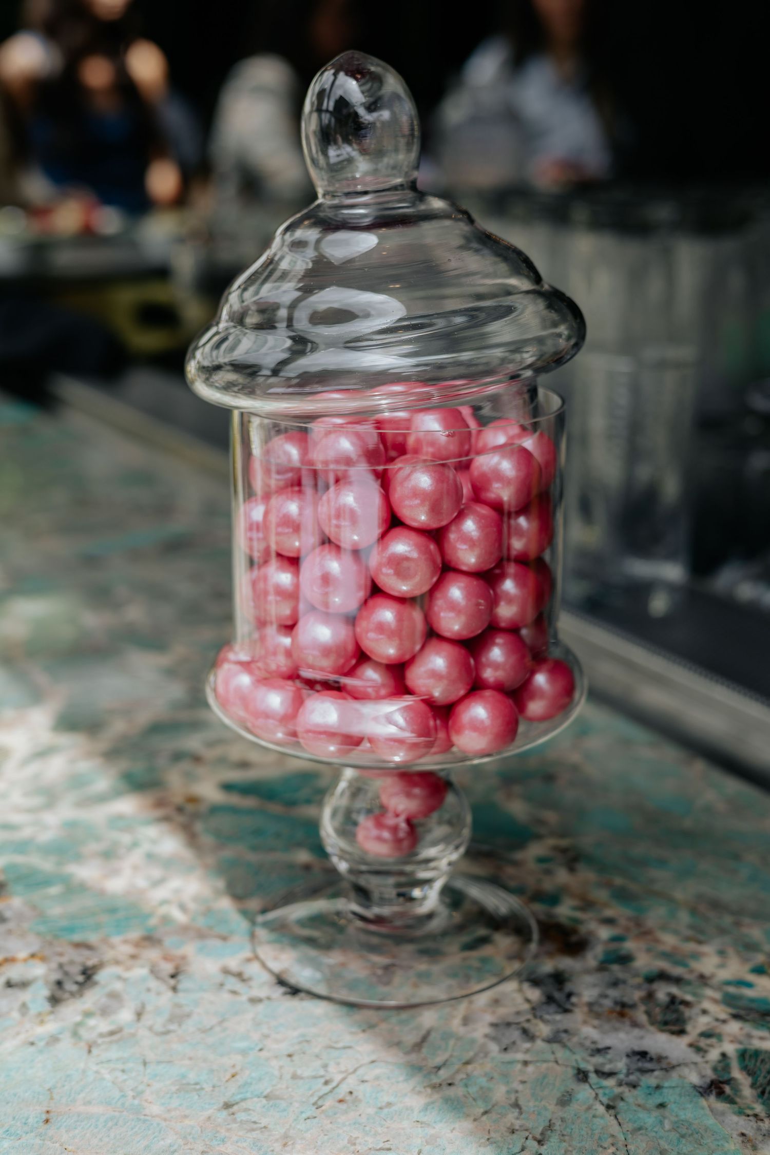 Glass apothecary jar filled with pink pearl candy balls on marble surface at wedding.