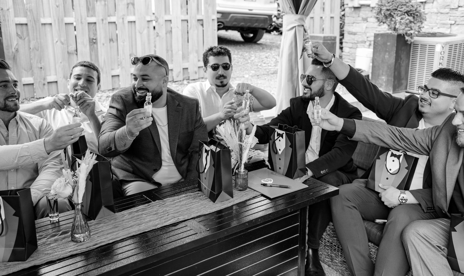Black and white photo of groomsmen raising glasses in a celebratory toast outdoors.