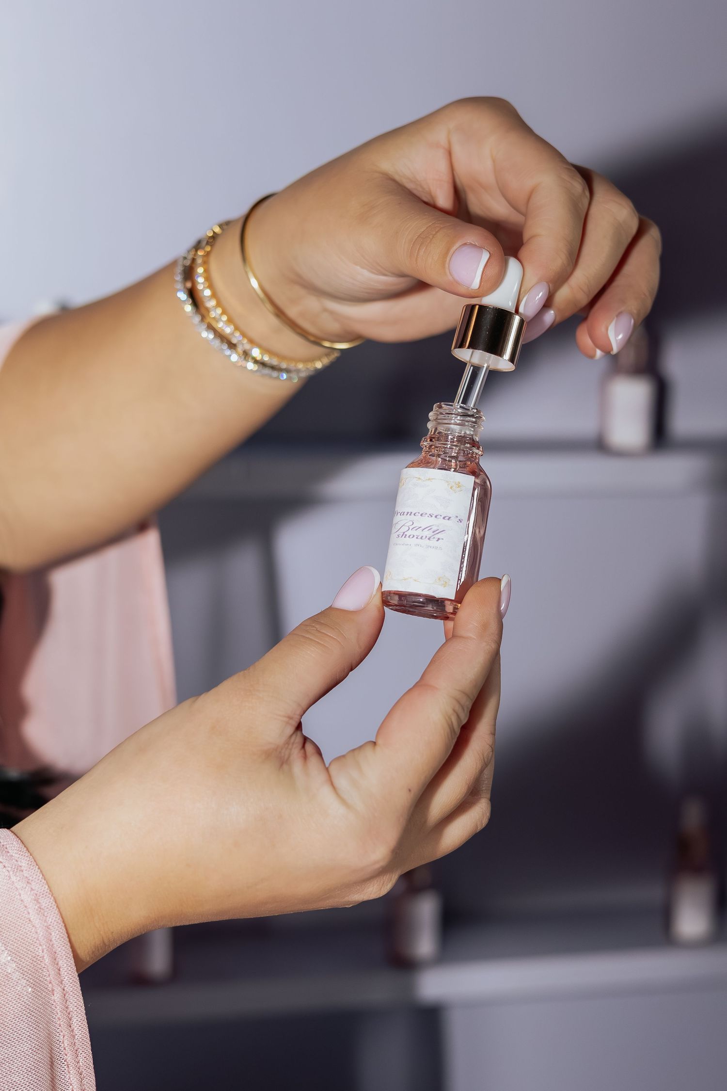 Hands holding a glass dropper bottle of serum with gold bracelets and neutral manicure.