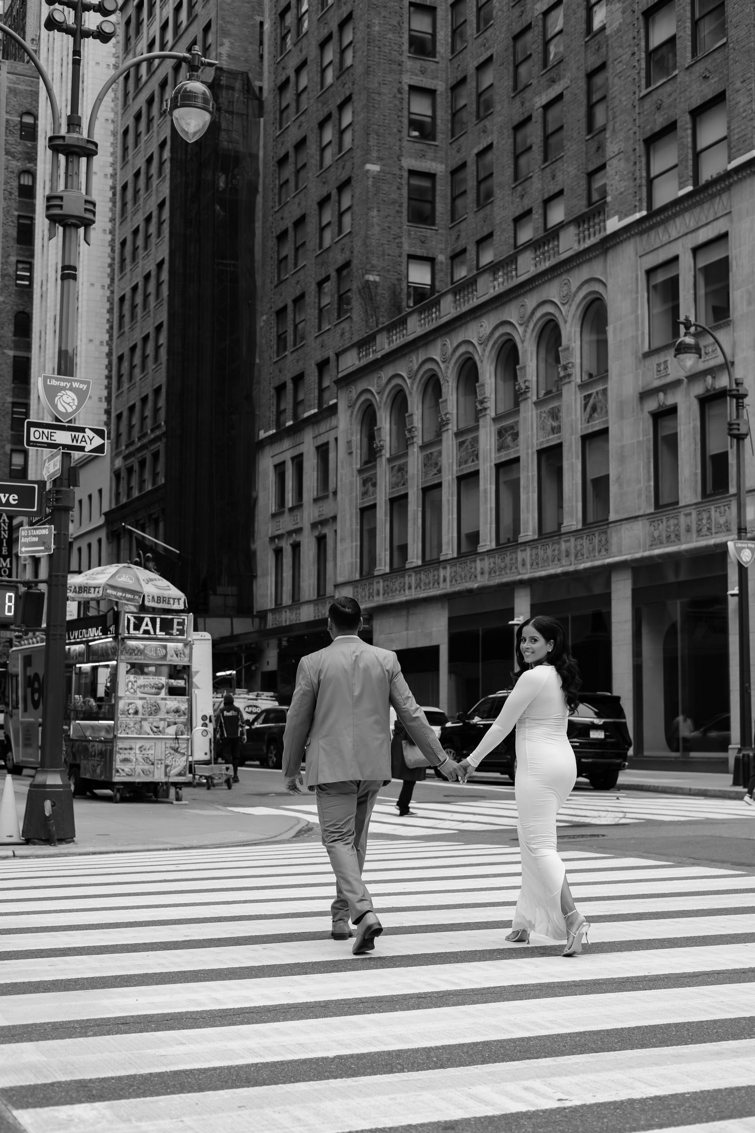 Black and white photo of couple holding hands crossing a New York City street.