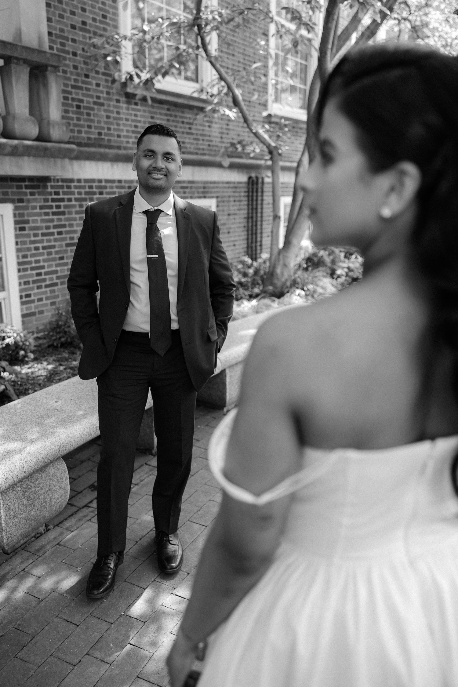 Black and white photo of smiling groom in suit looking at bride in white wedding dress.