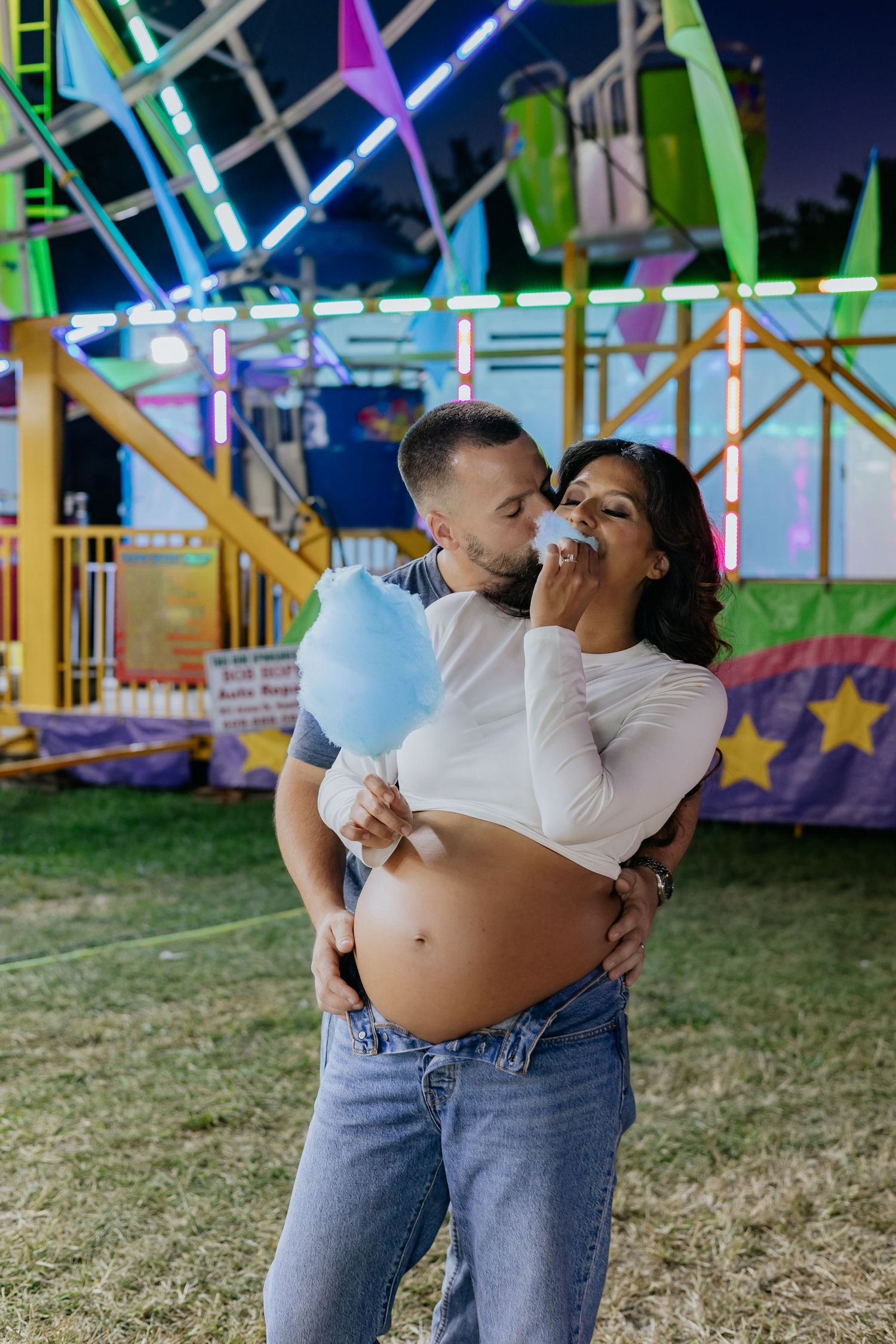 Couple sharing blue cotton candy at a colorful carnival at night.