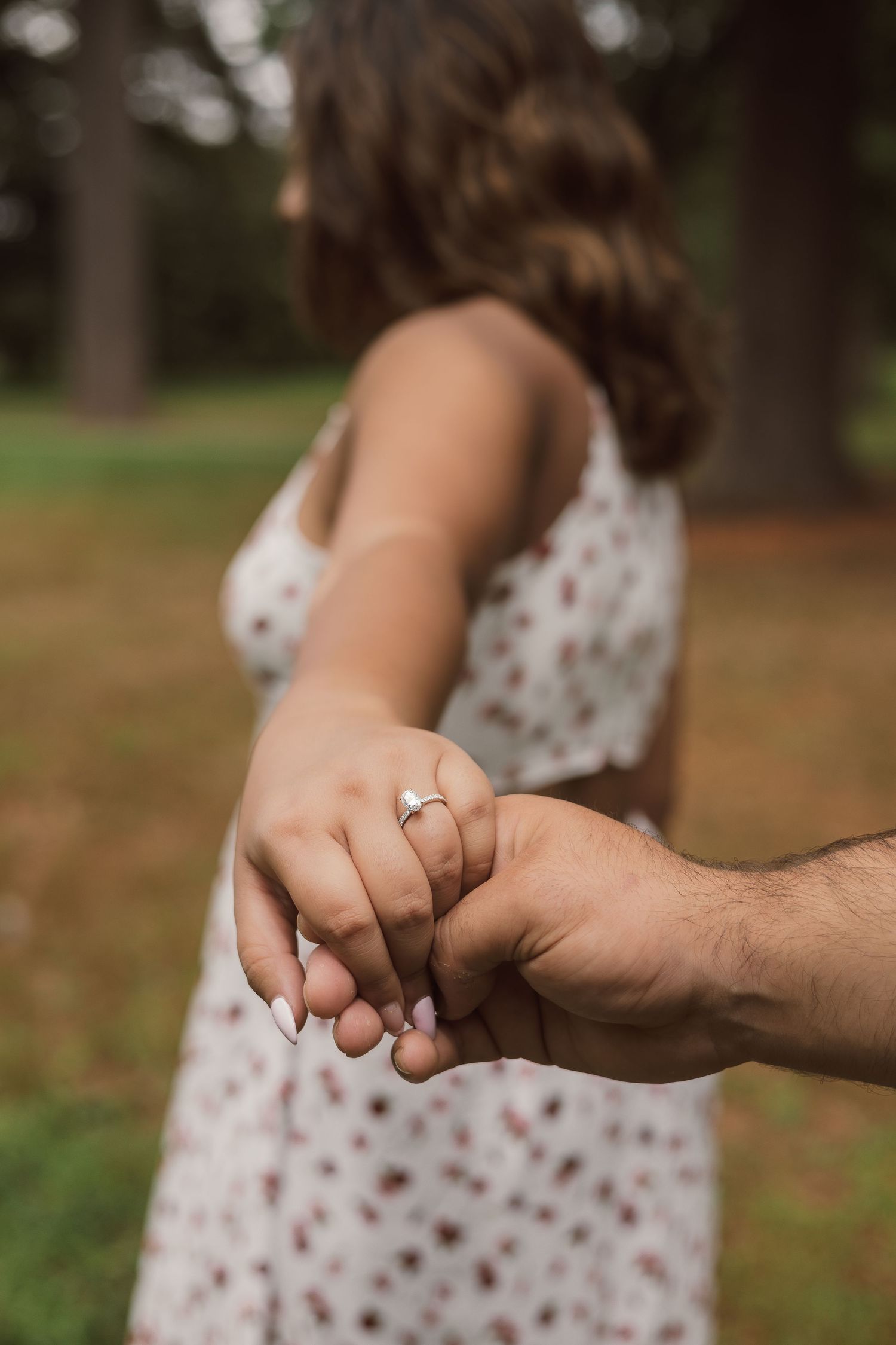 Close-up of an engaged couple holding hands showcasing a diamond engagement ring outdoors.