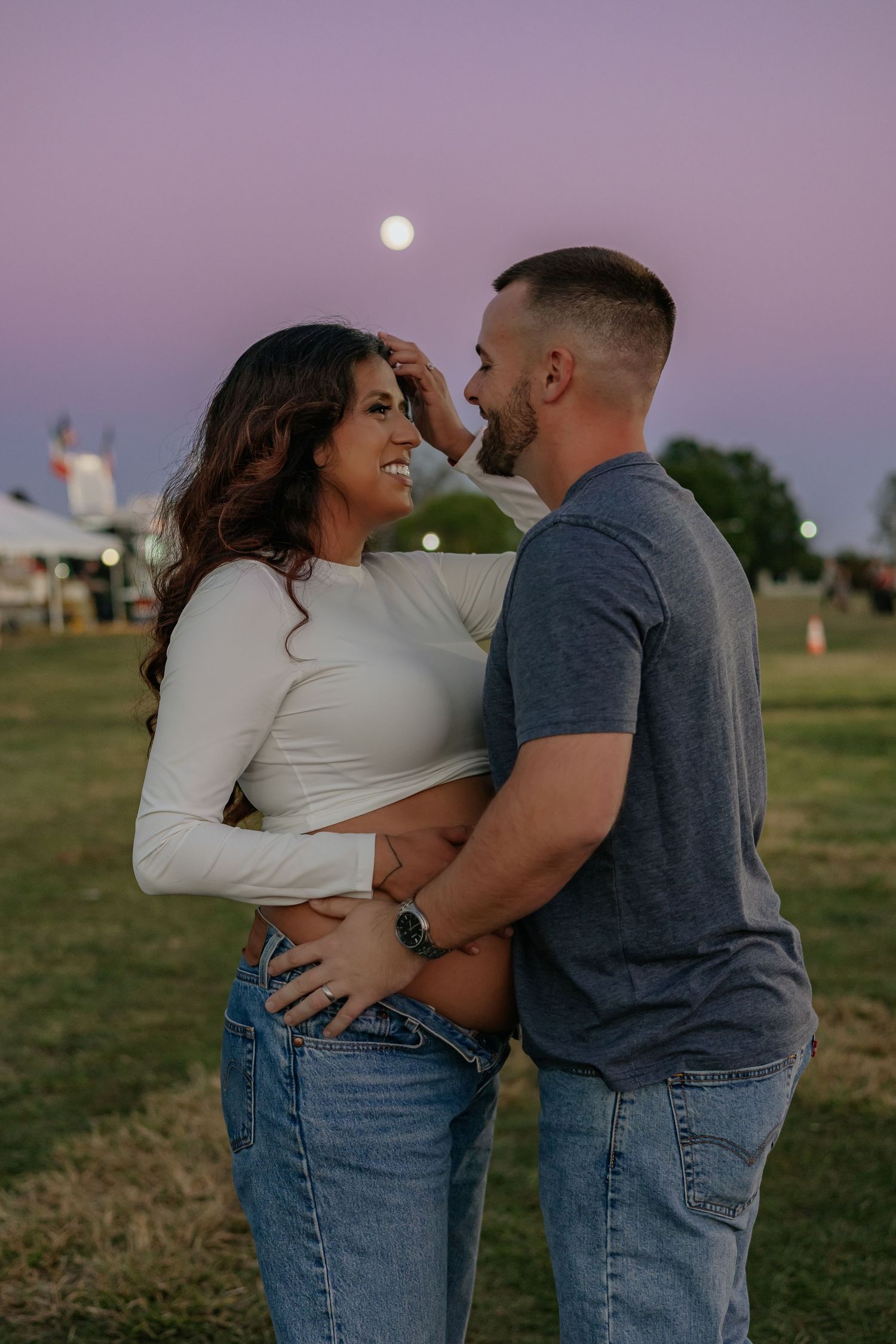 Couple embracing romantically at dusk with full moon behind them.