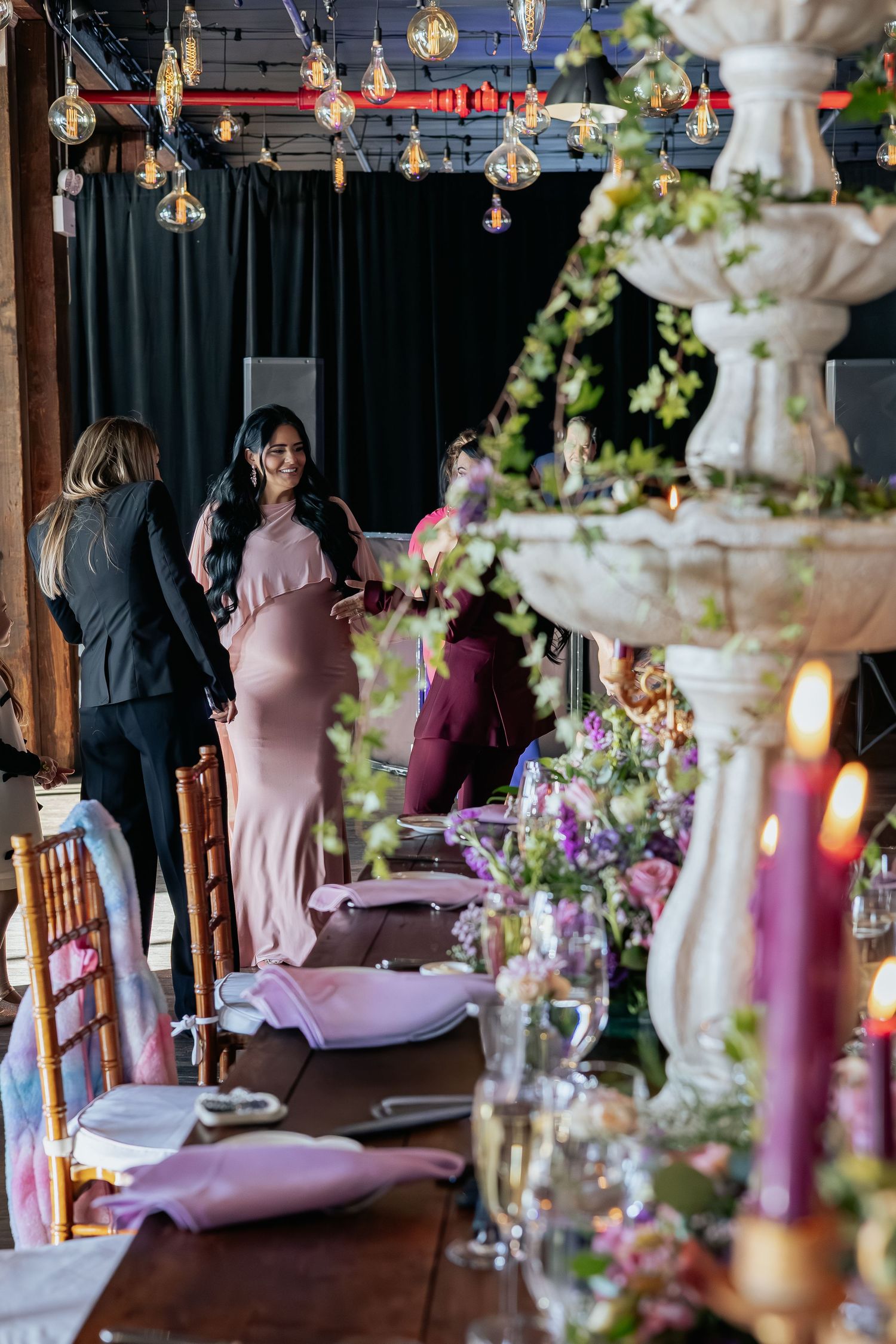 Pregnant woman in blush pink gown socializing near ornate fountain centerpiece at elegant baby shower event.