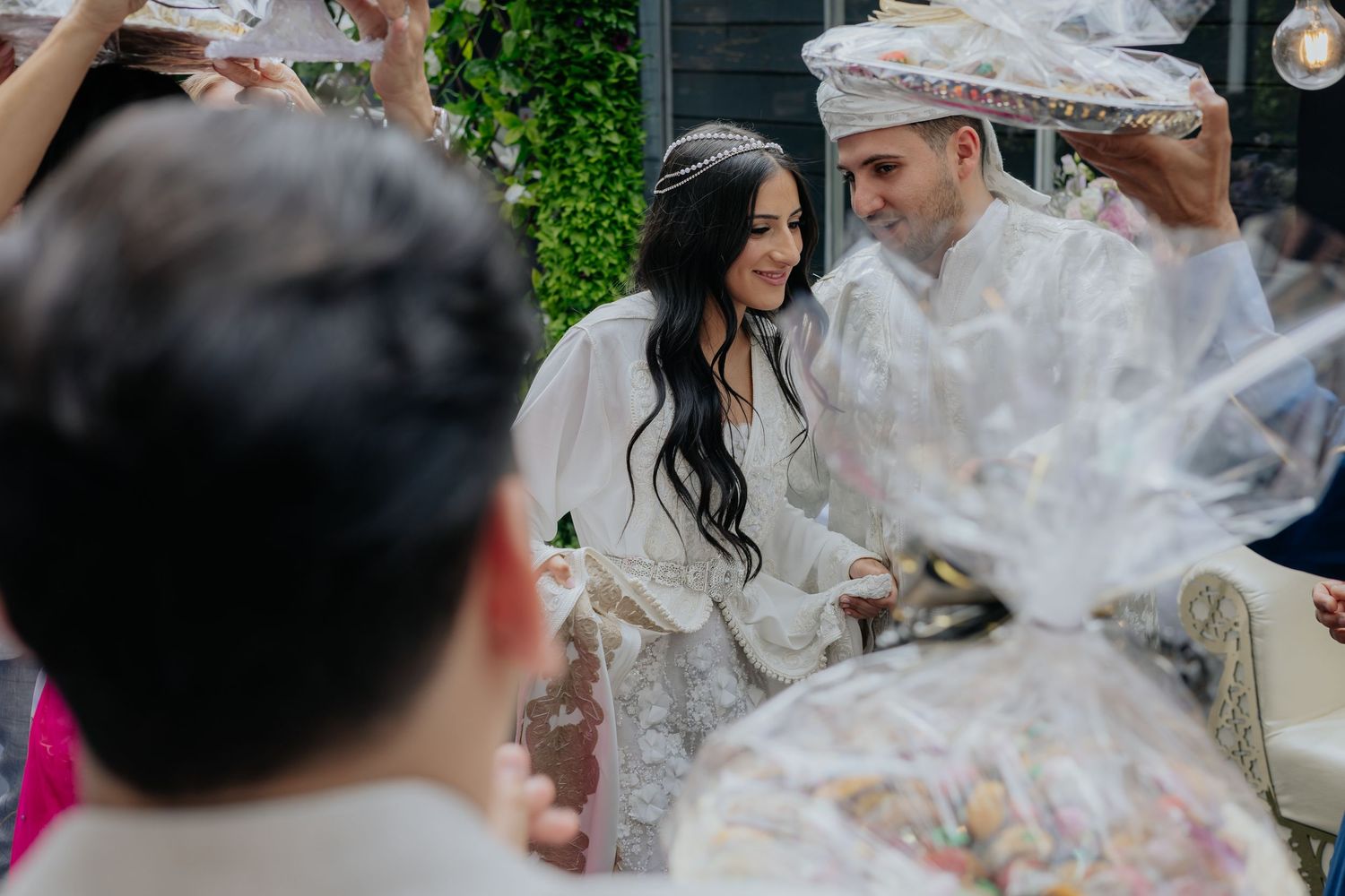 Bride and groom in matching white Moroccan attire greeting guests with candy gift bags.