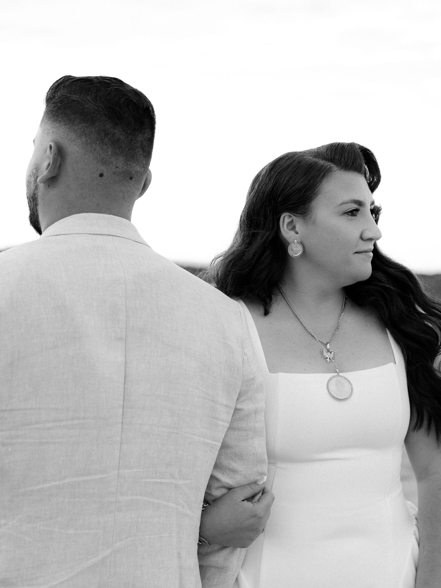 Black and white photo of a bride in white dress and groom in linen suit at an outdoor wedding ceremony.