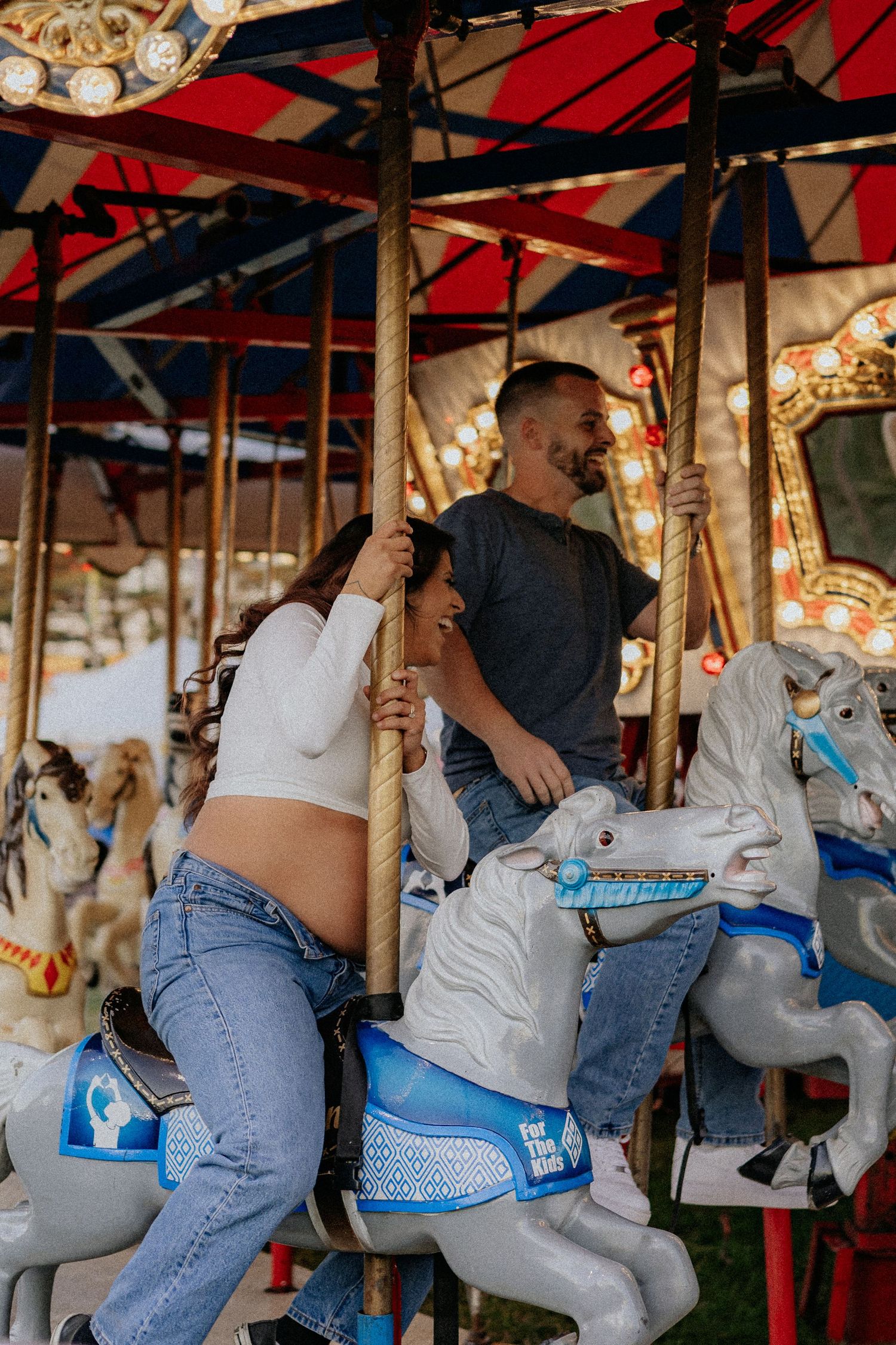 Happy couple riding carousel horses at a colorful carnival fair.