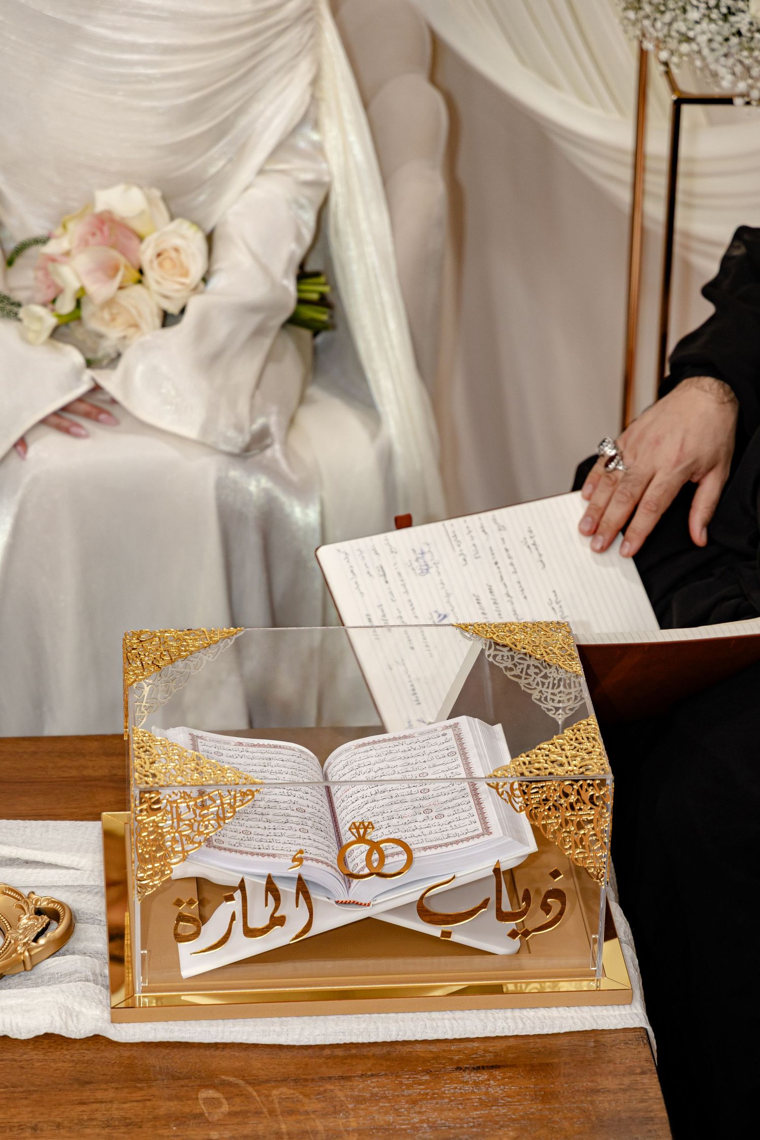 Islamic wedding ceremony with open Quran on ornate gold stand as couple sits in background.