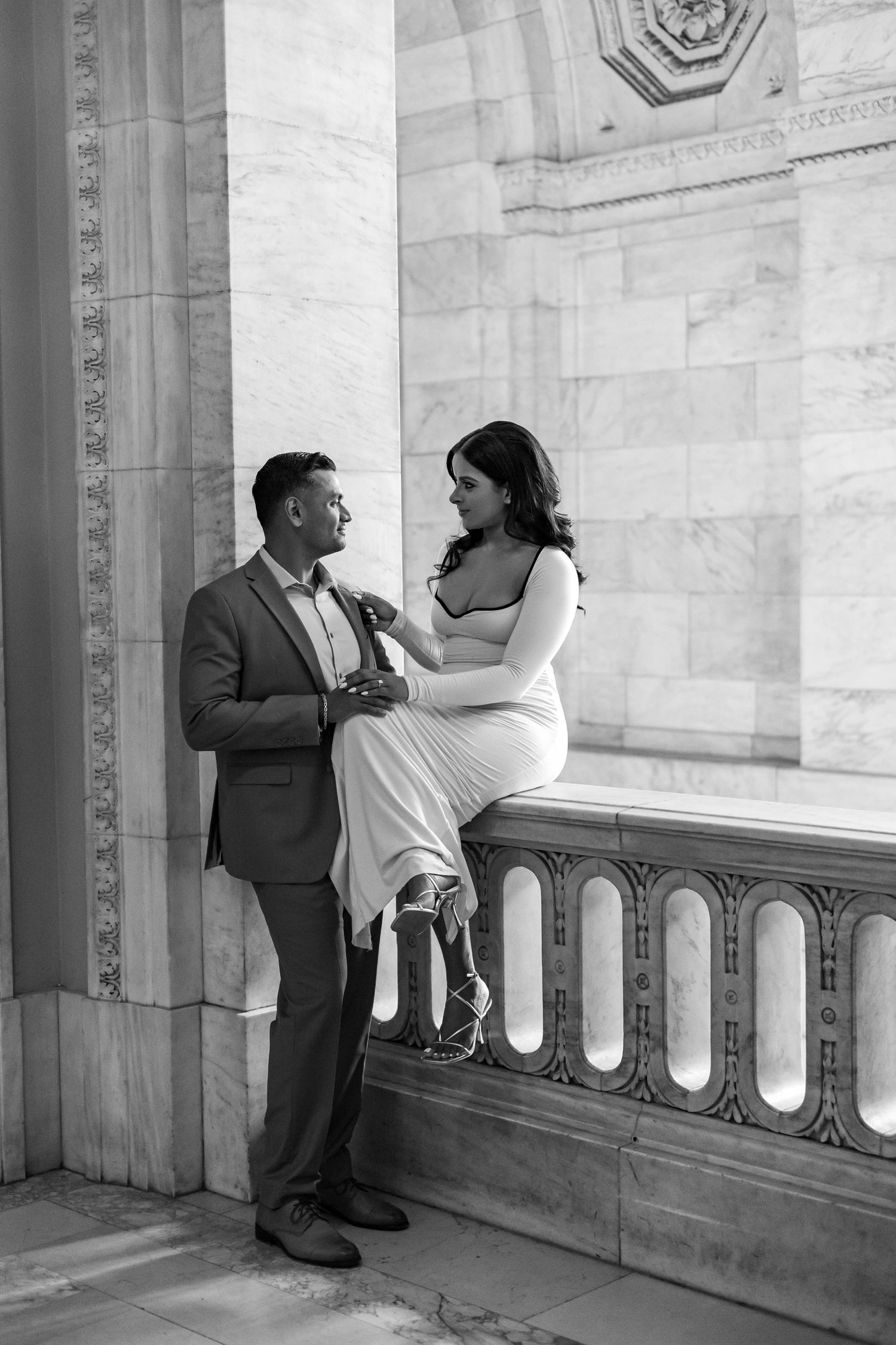 Black and white photo of couple sharing intimate moment by ornate stone columns.