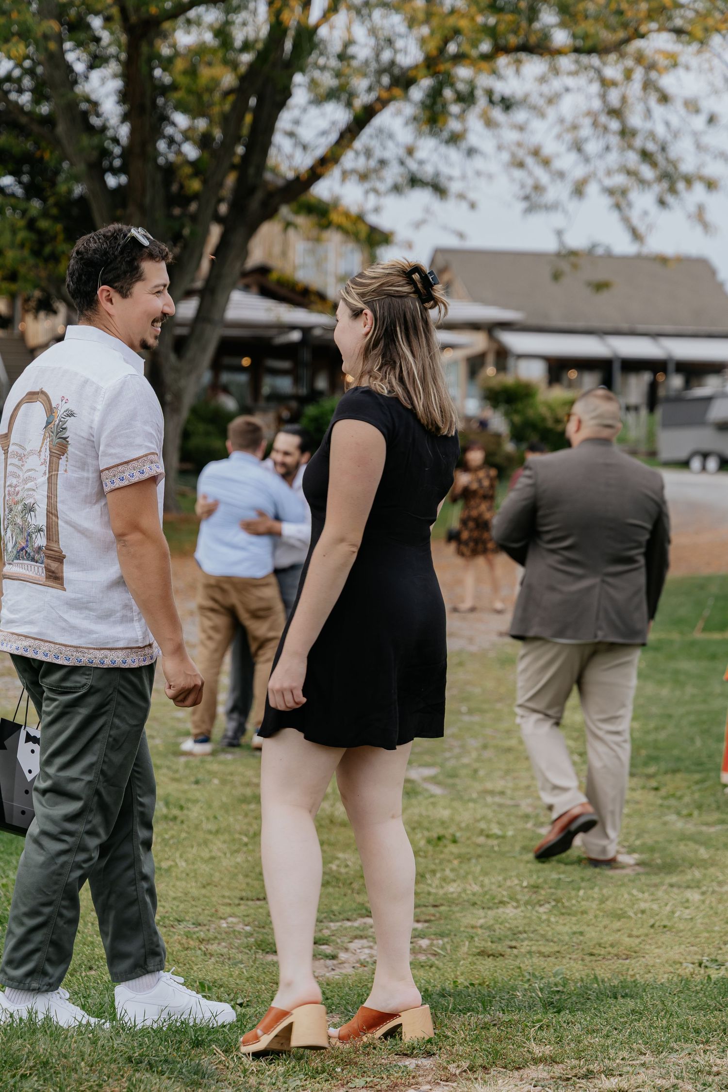 A couple holds hands while walking on grass at an outdoor gathering event.