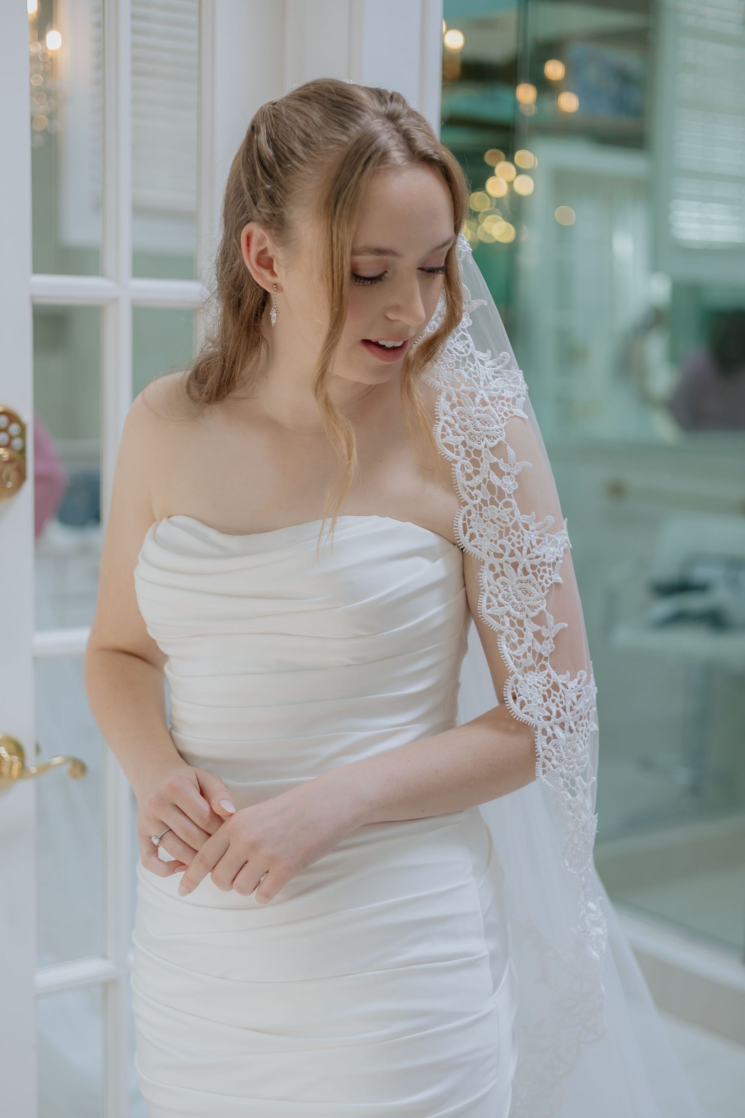 Beautiful blonde bride in strapless white wedding dress with lace veil looking down elegantly.