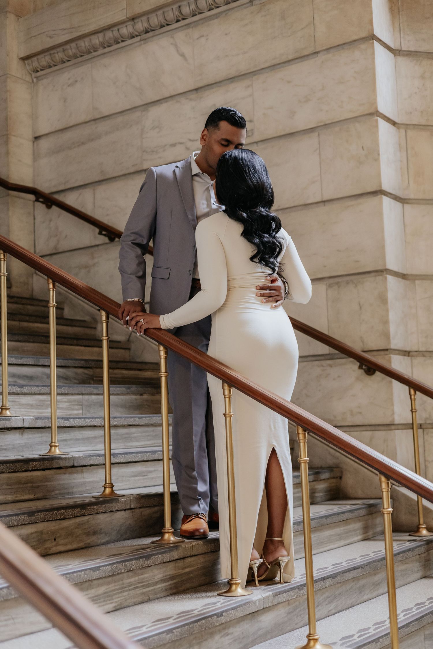 Couple sharing a kiss on ornate marble staircase with brass railings.