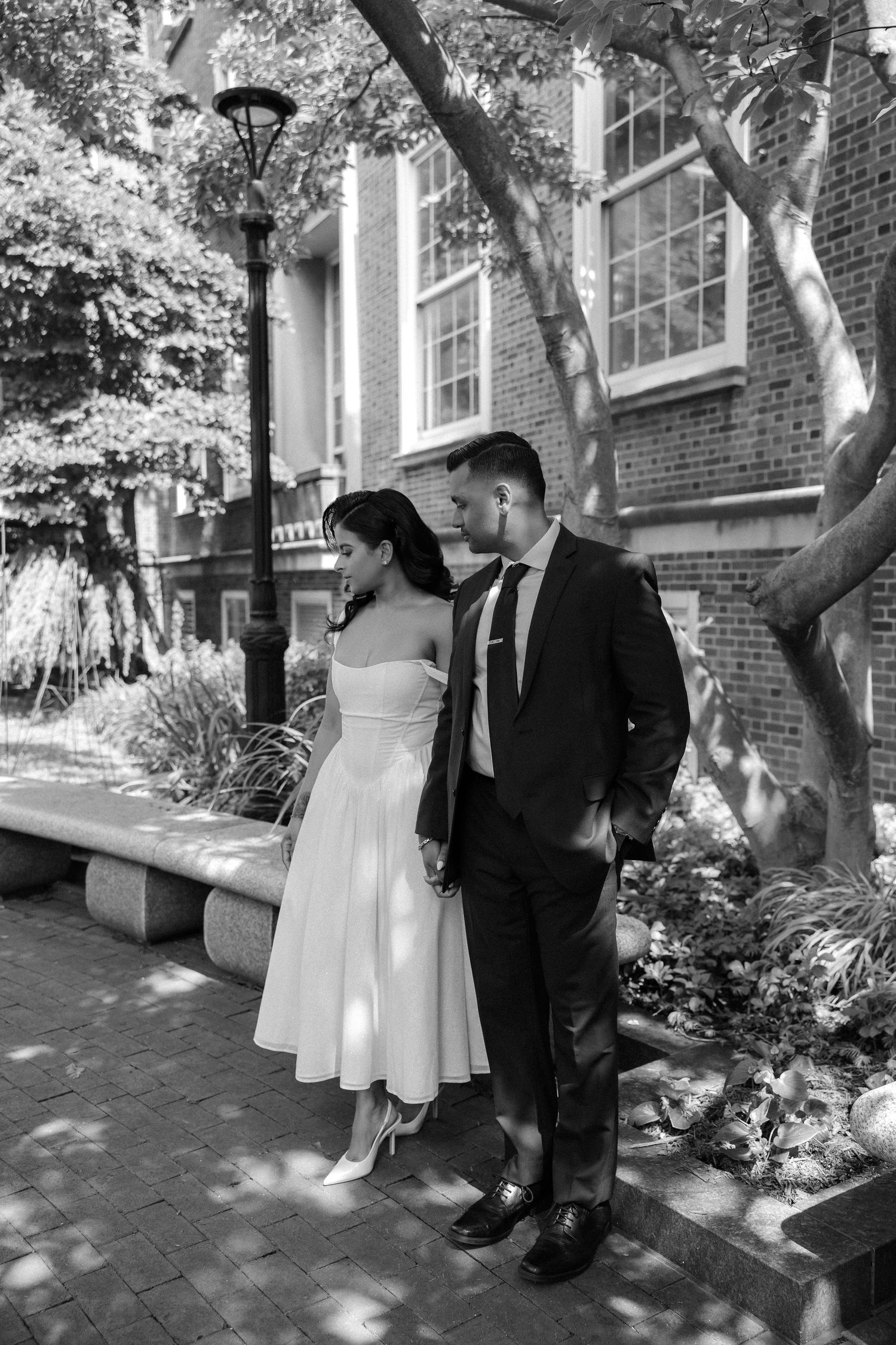 Black and white photo of a bride and groom holding hands and gazing at each other outdoors.