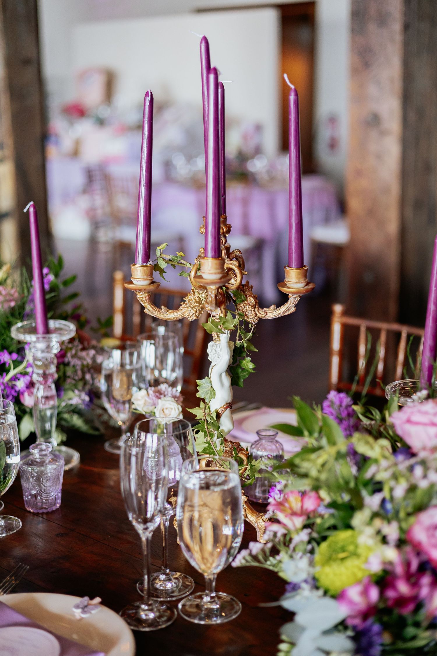 Gold candelabra with purple taper candles surrounded by colorful flowers on a decorated table.