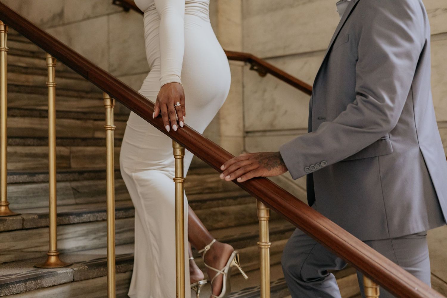 Close-up of couple holding hands on brass railing of a marble staircase.