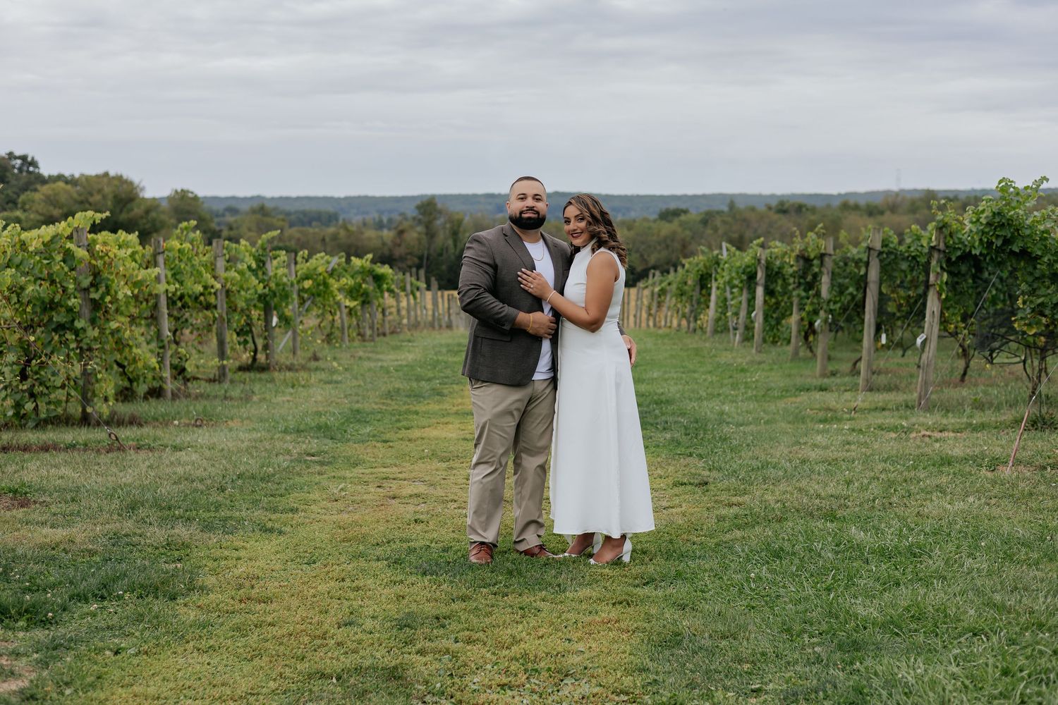 Couple embraces in a scenic vineyard with rolling hills in the background on their engagement shoot.
