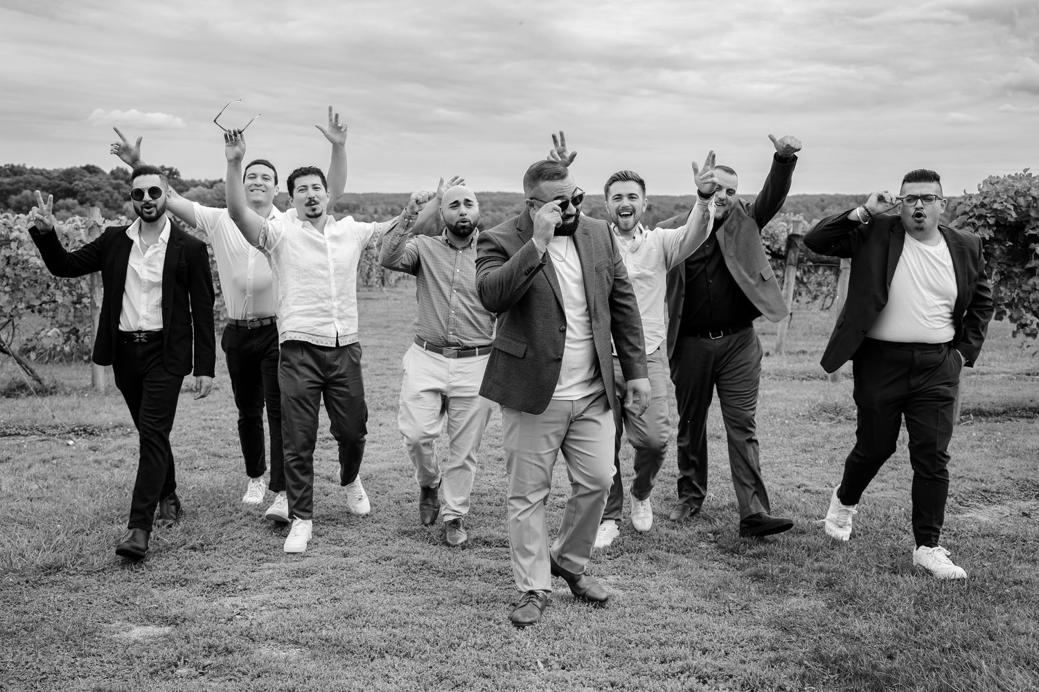 Black and white photo of seven men jumping and celebrating joyfully at an outdoor vineyard wedding.
