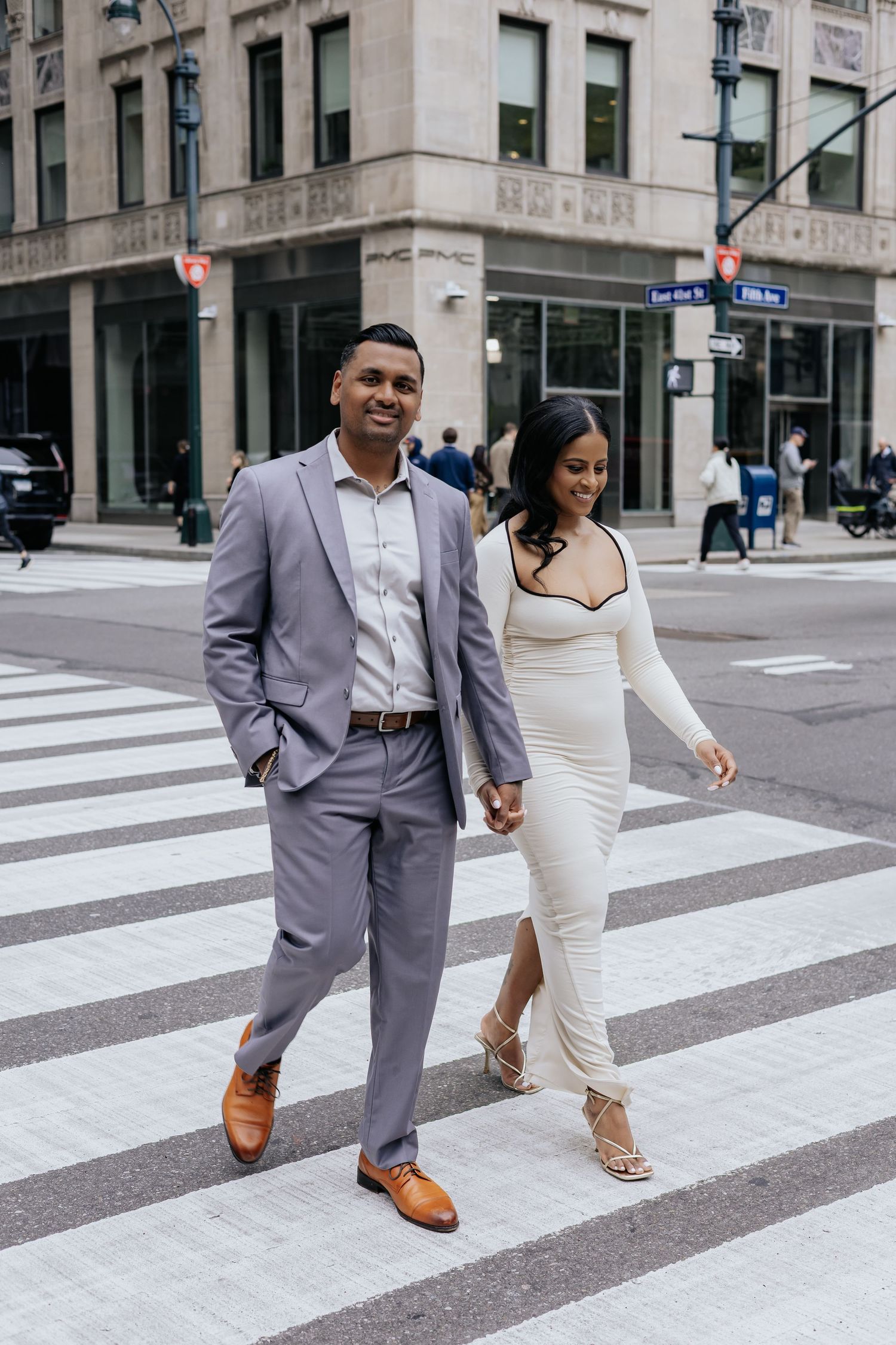 Stylish engaged couple holding hands while crossing a city street crosswalk together.