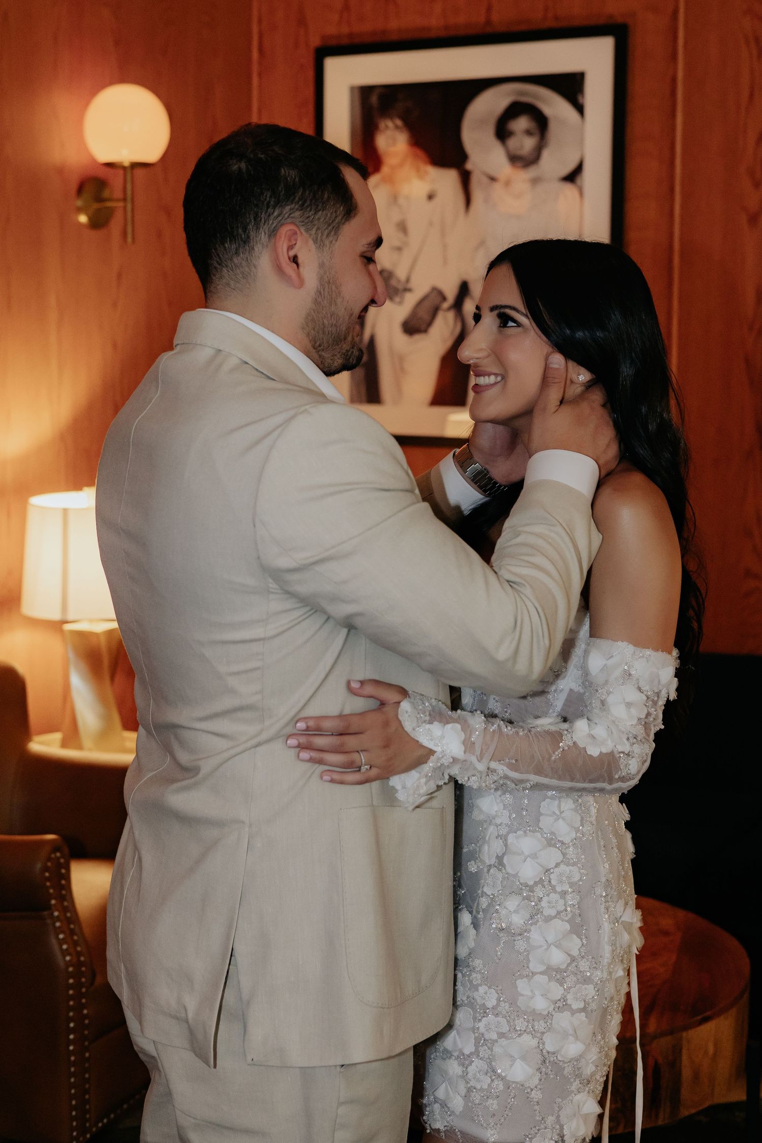 Groom tenderly cupping brides face as they share an intimate moment in a warmly lit room.