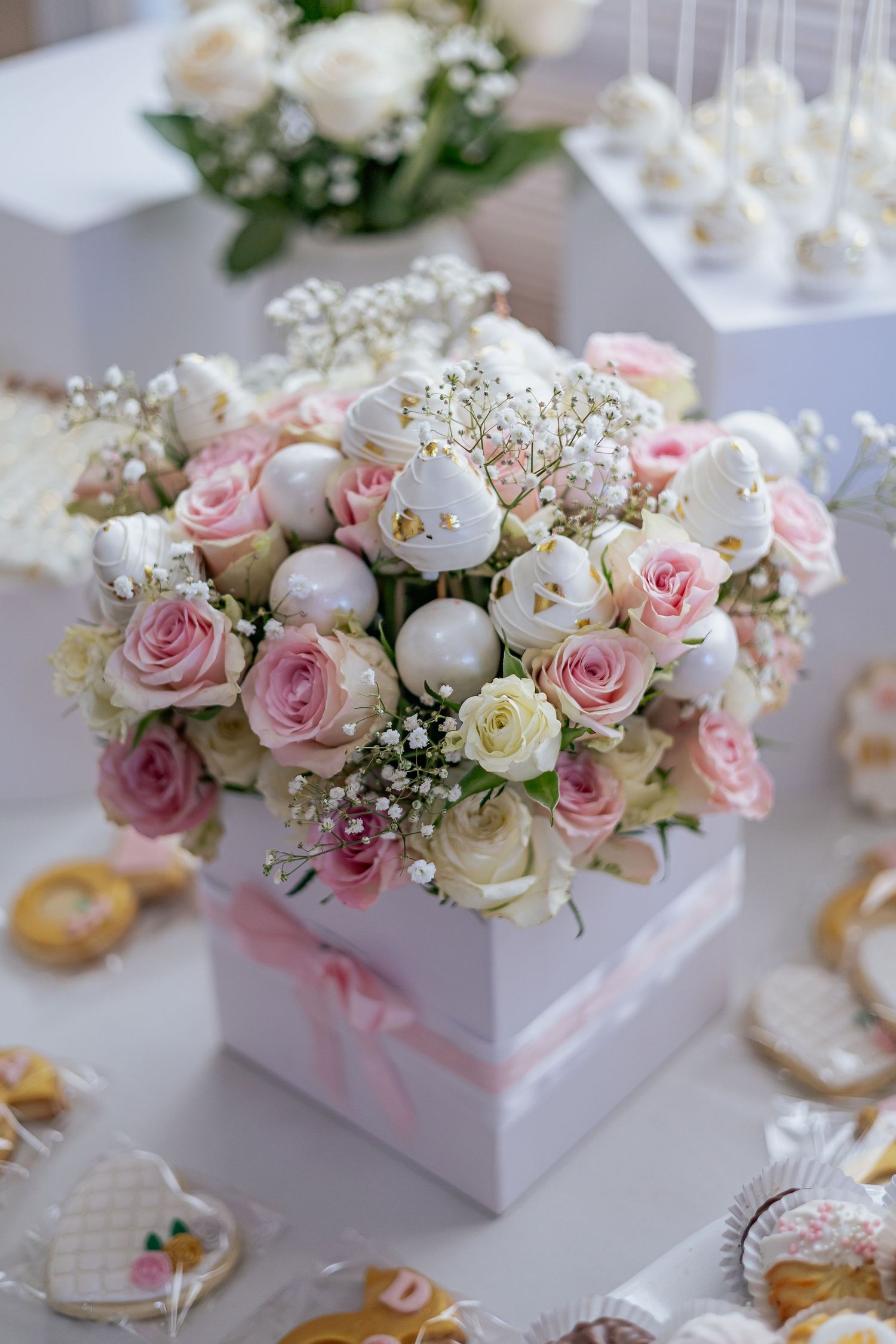 Beautiful wedding centerpiece with pink and white roses, macarons, and baby's breath in a white gift box.
