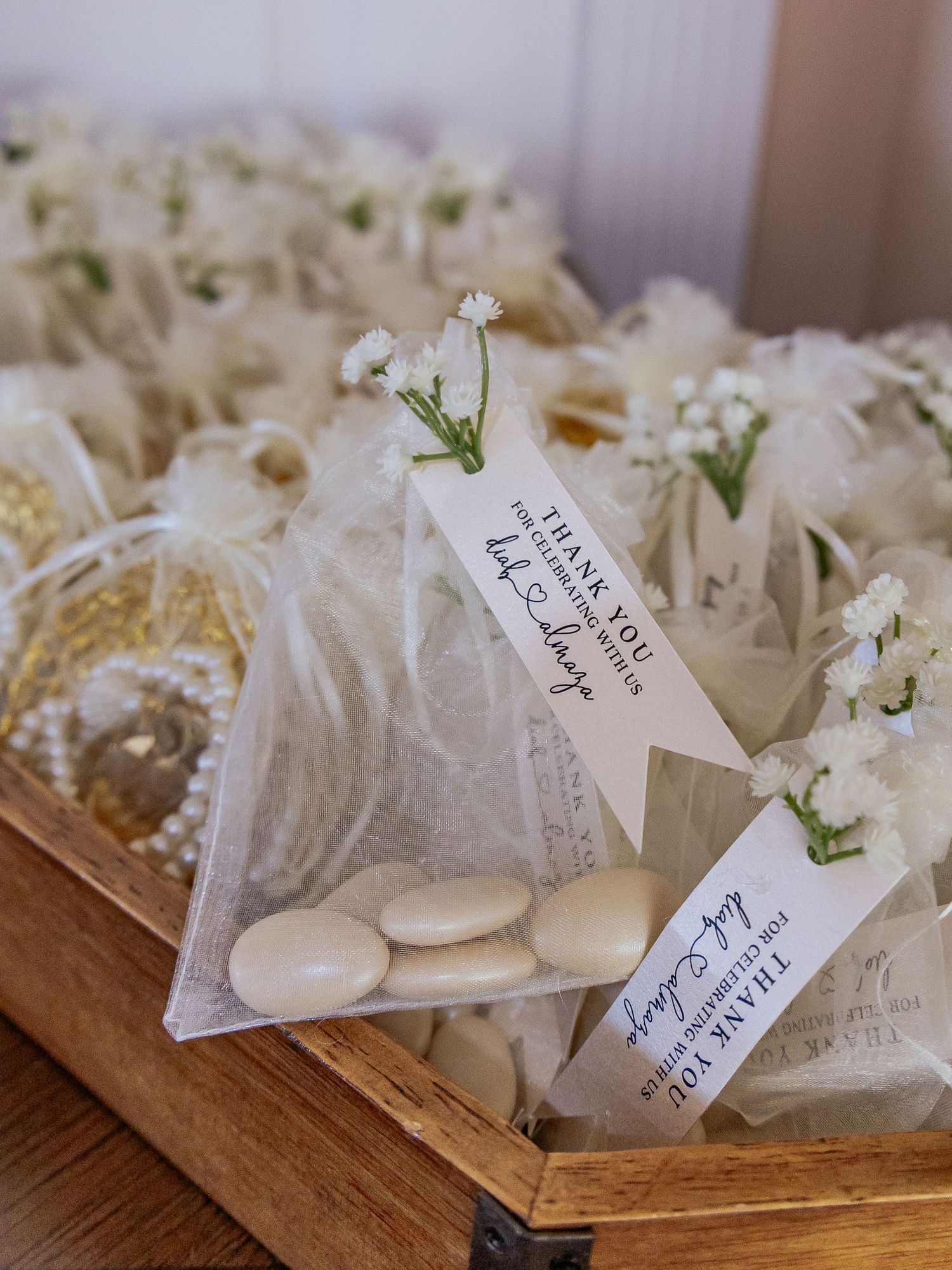 Elegant white organza wedding favor bags filled with Jordan almonds and baby's breath flowers in a wooden box.