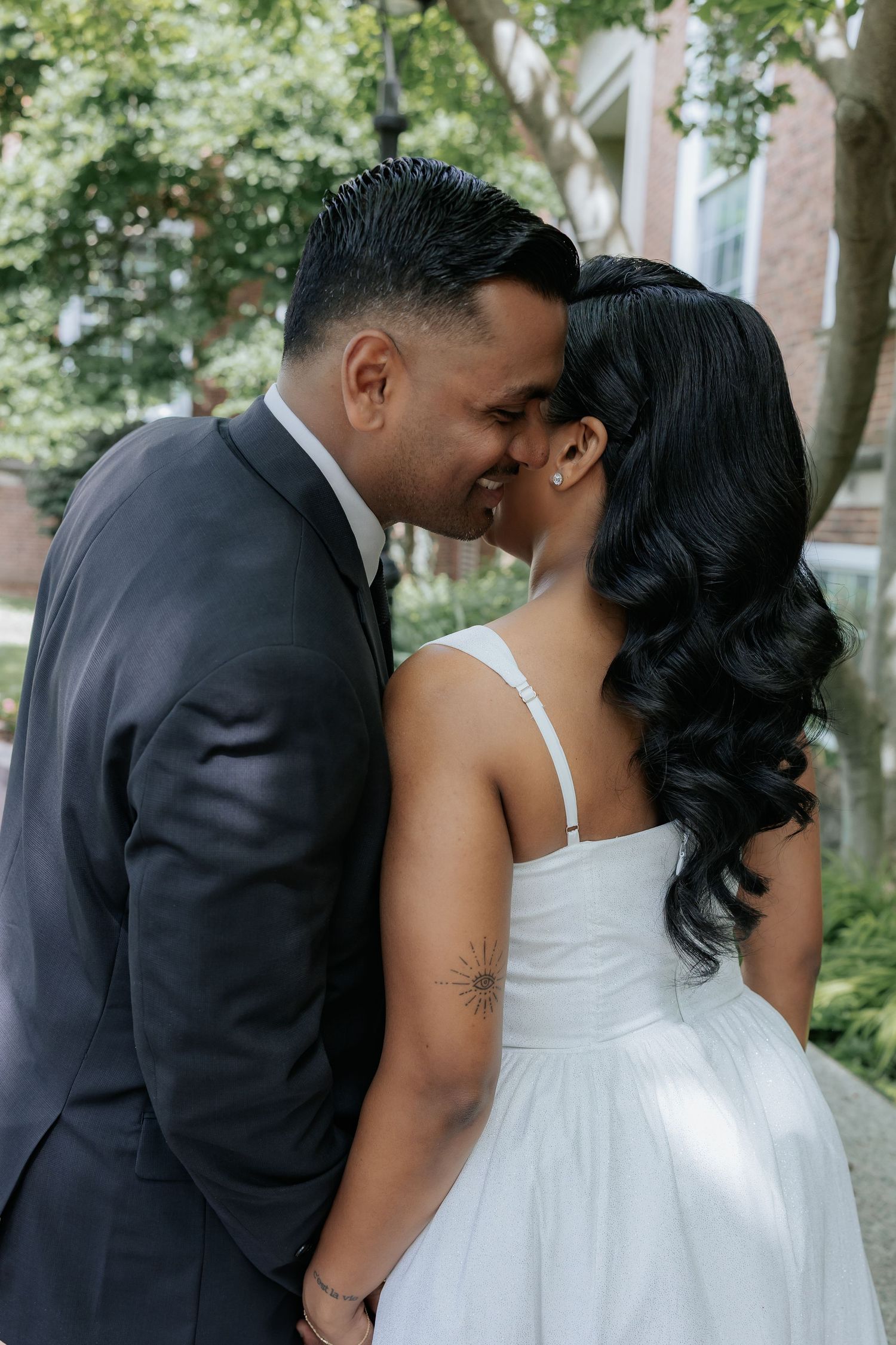 Smiling bride and groom sharing a close romantic moment kissing outdoors on wedding day.