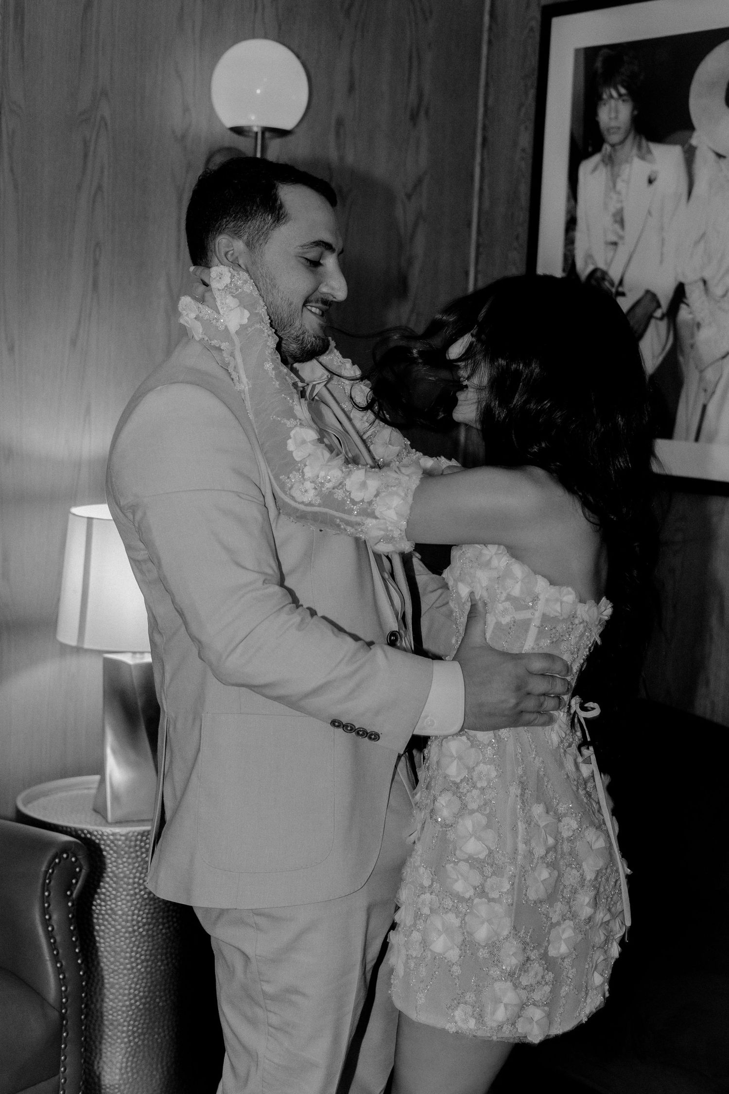 Black and white photo of bride and groom laughing and embracing in a stylish indoor setting.