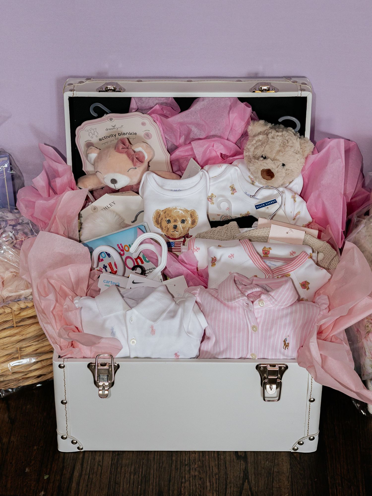 Pink baby shower gift trunk filled with teddy bears, onesies, and Ralph Lauren baby items.