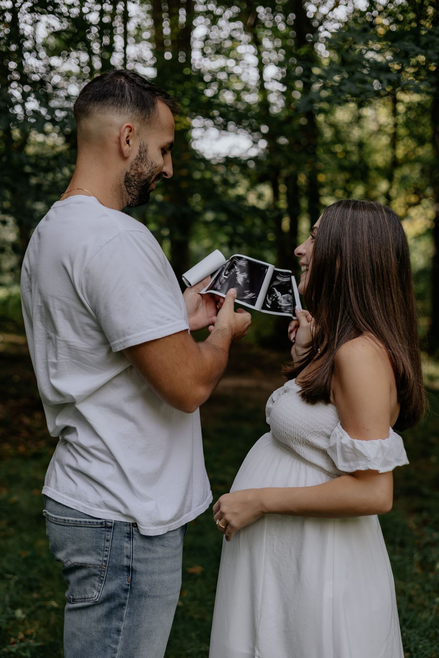 Happy expecting couple viewing ultrasound photos together outdoors in a green wooded setting.