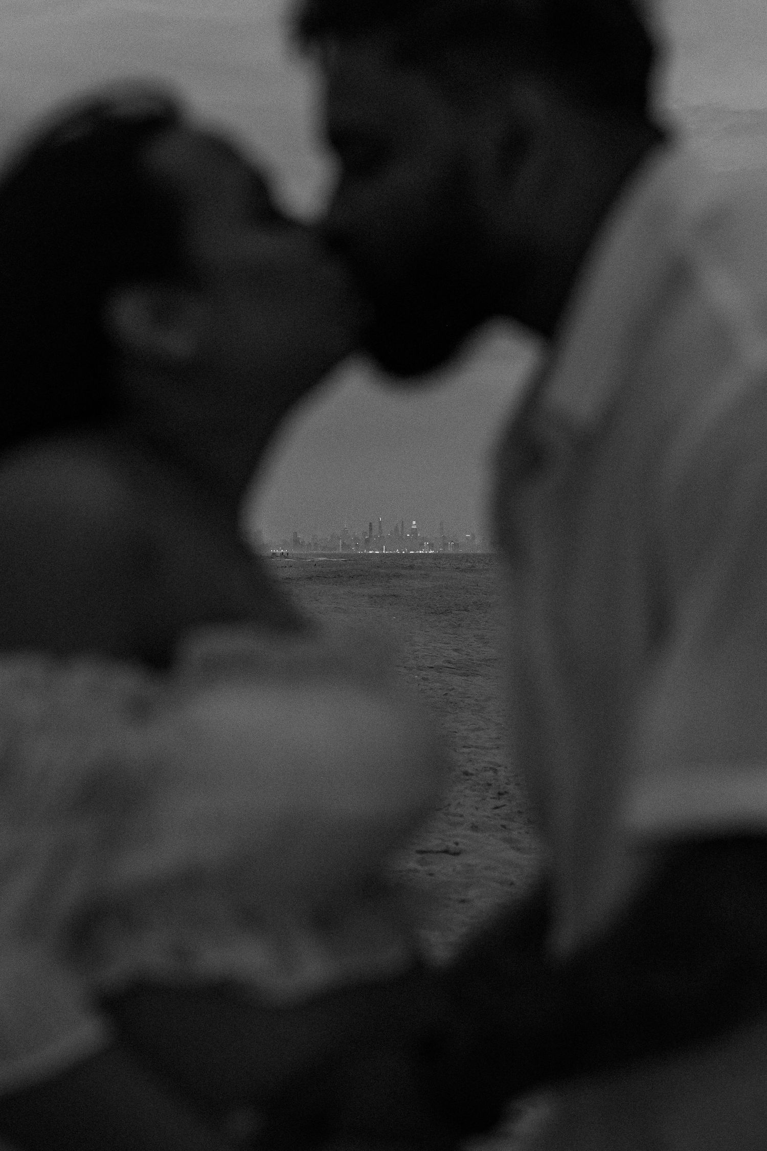 Romantic black and white photo of couple kissing on beach at twilight.