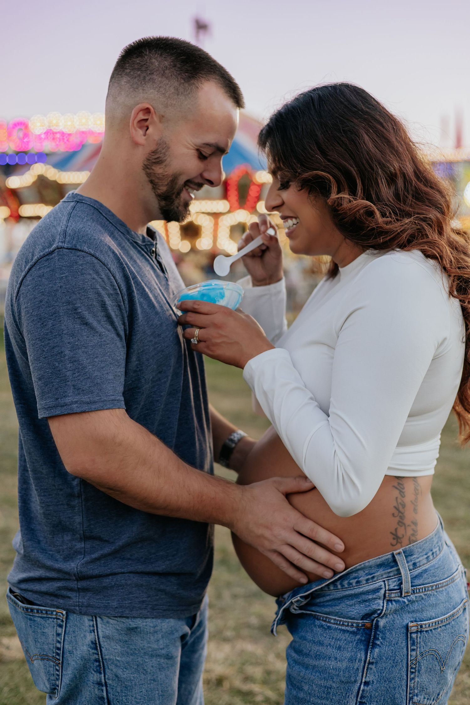 Smiling pregnant couple sharing blue shaved ice at a fairground.
