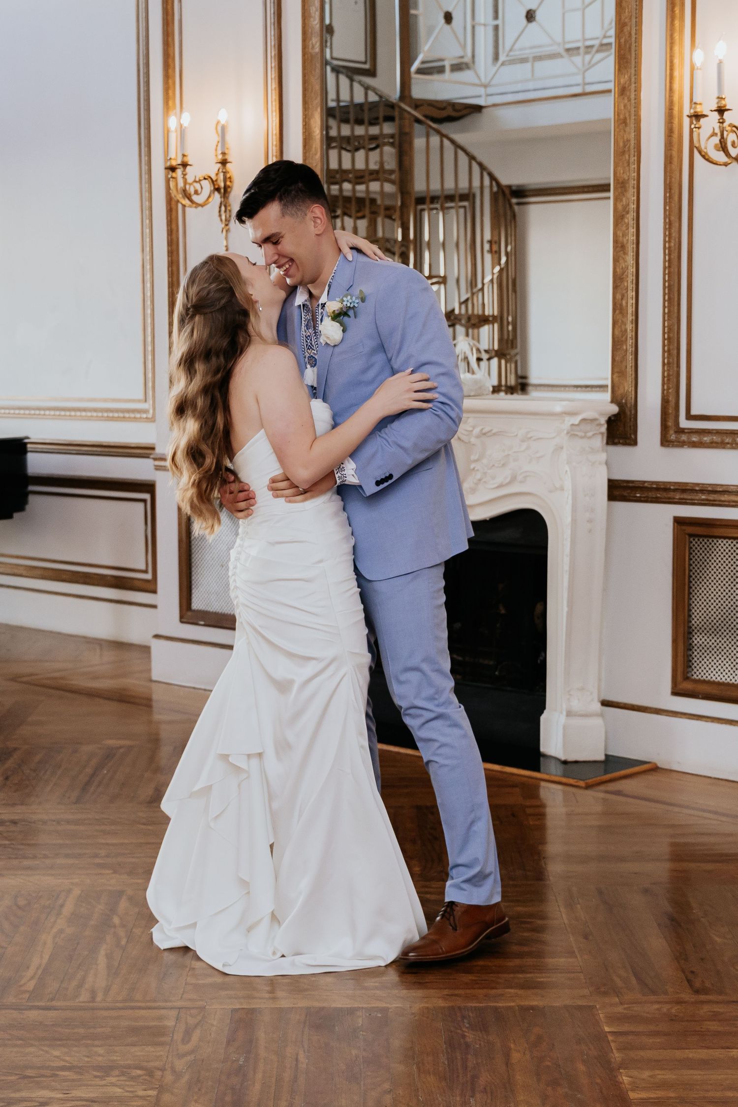 Bride and groom share a joyful embrace while dancing in an elegant white and gold ballroom.