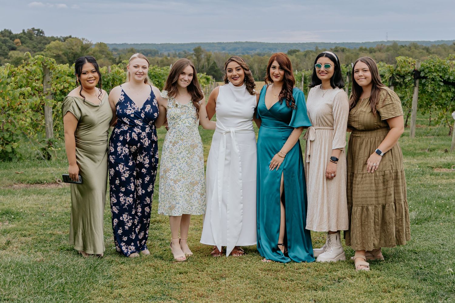 Seven women posing together in a vineyard at an outdoor bridal shower celebration.