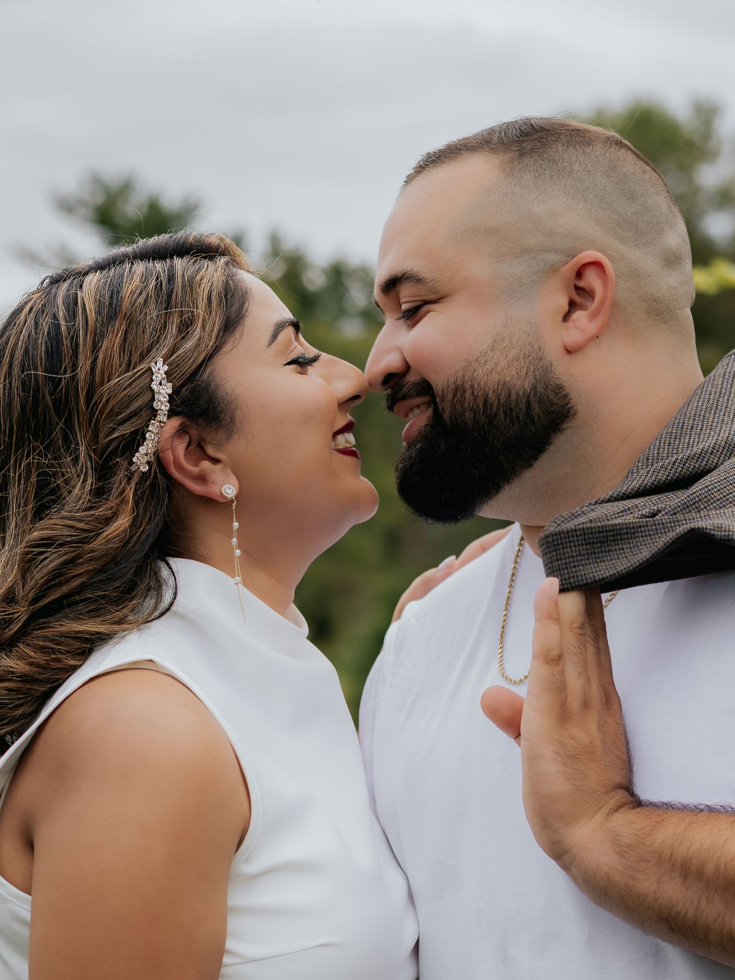 Romantic close-up of smiling couple almost kissing outdoors, woman wearing crystal earrings.