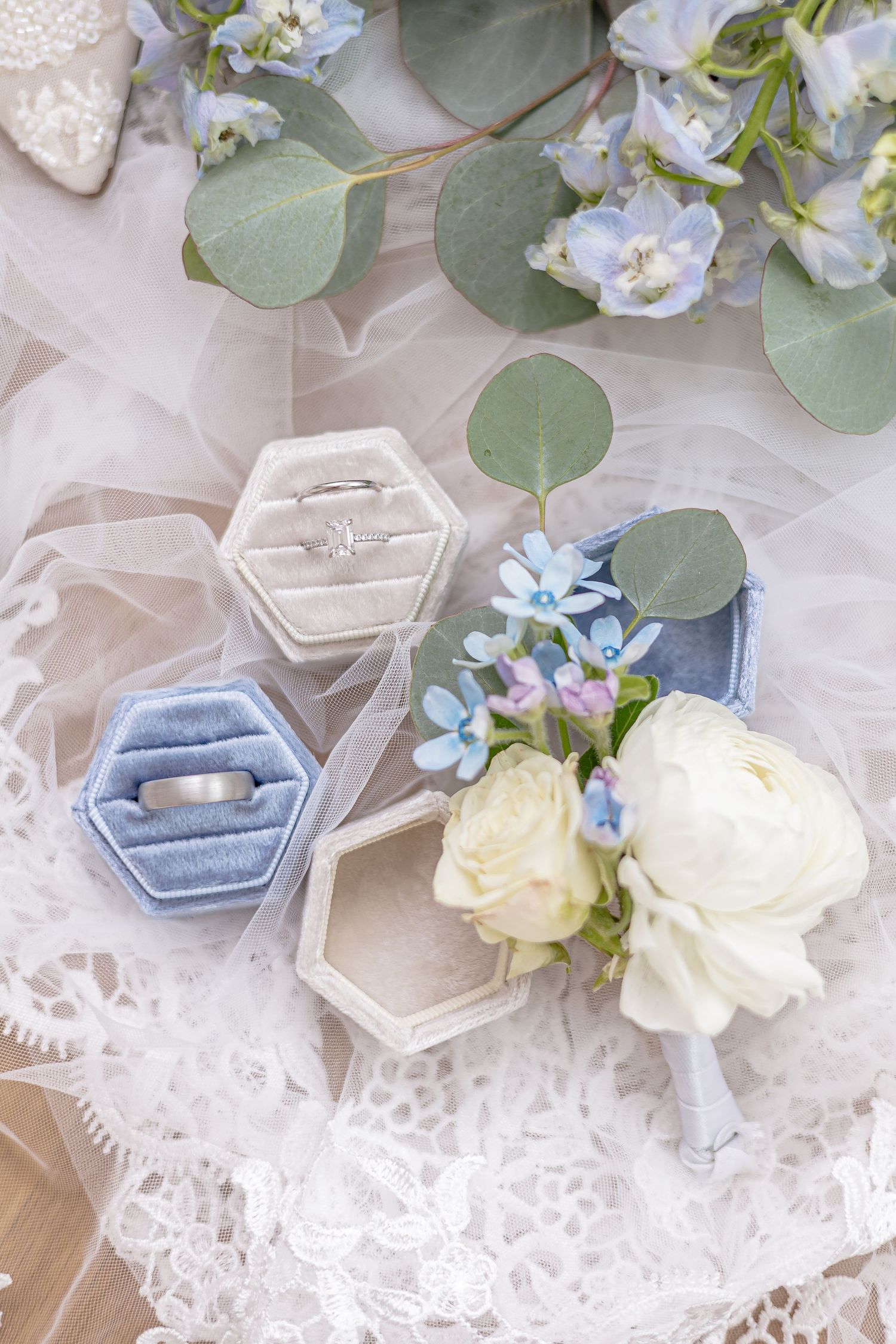 Close-up of two hexagonal velvet ring boxes with wedding bands and white boutonniere.