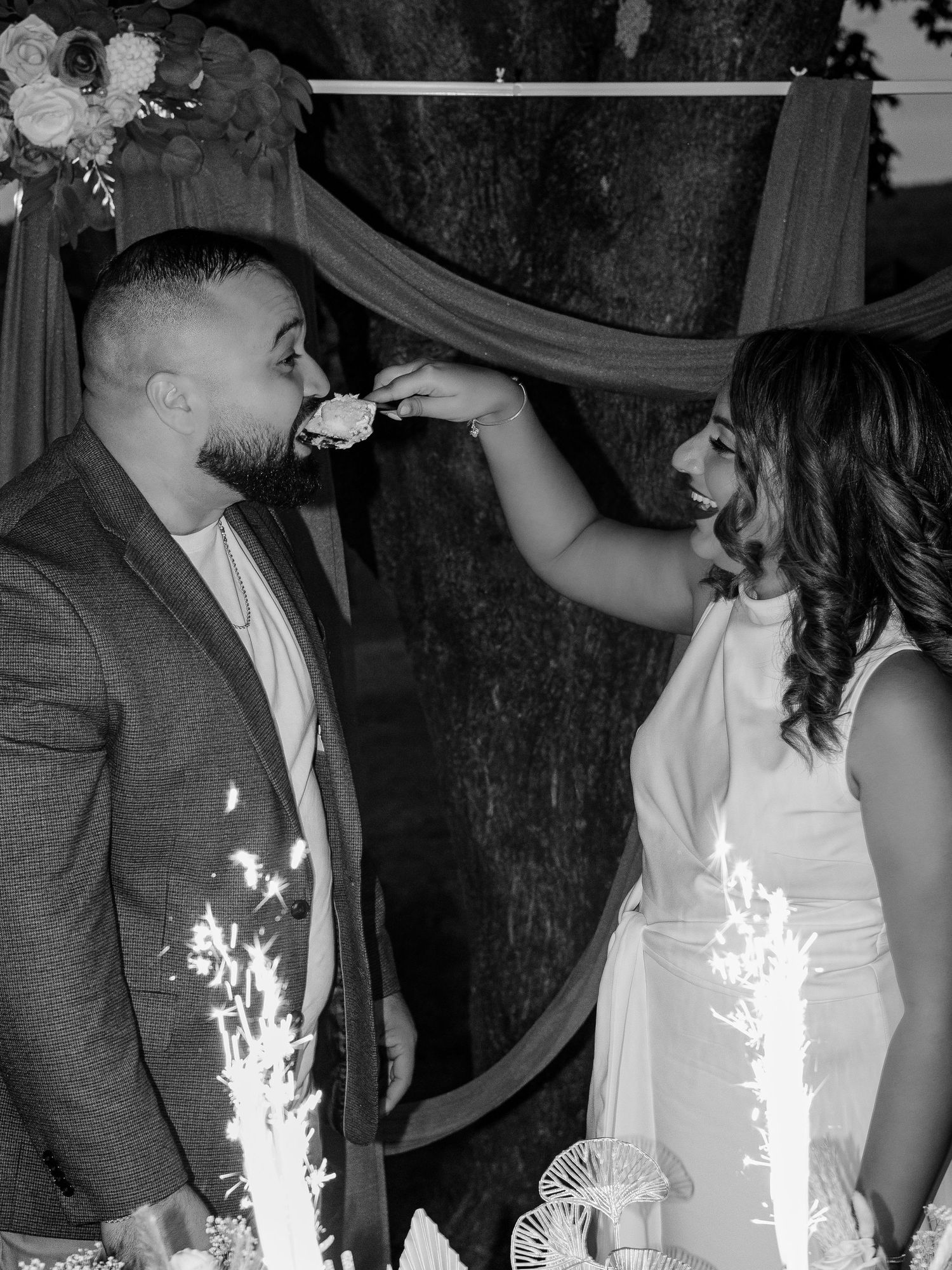 Black and white photo of bride feeding groom cake at outdoor engagement party.